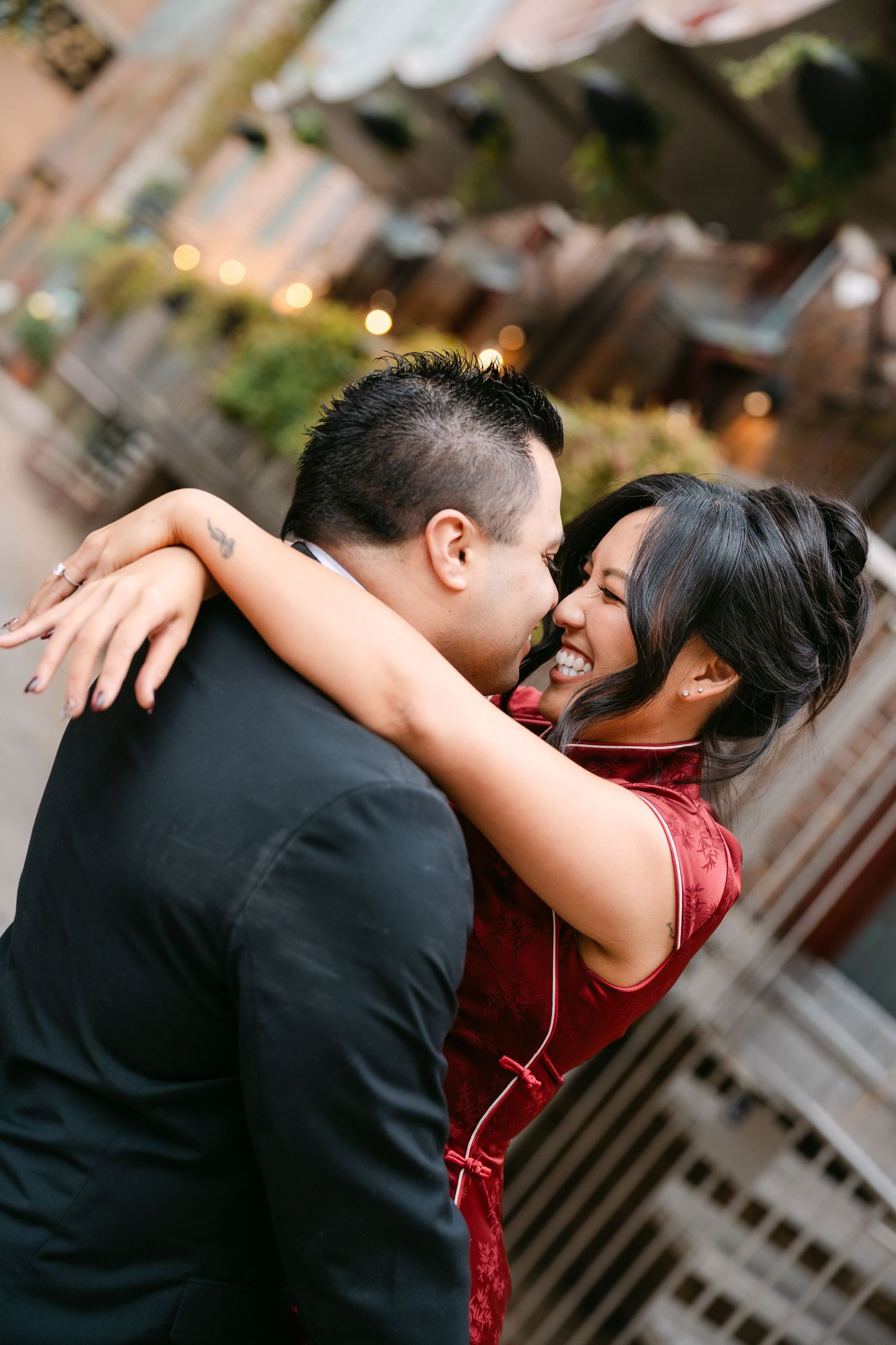 Laughing couple embracing outdoors, woman in red qipao dress hugging mans neck at The Rocks, Sydney.