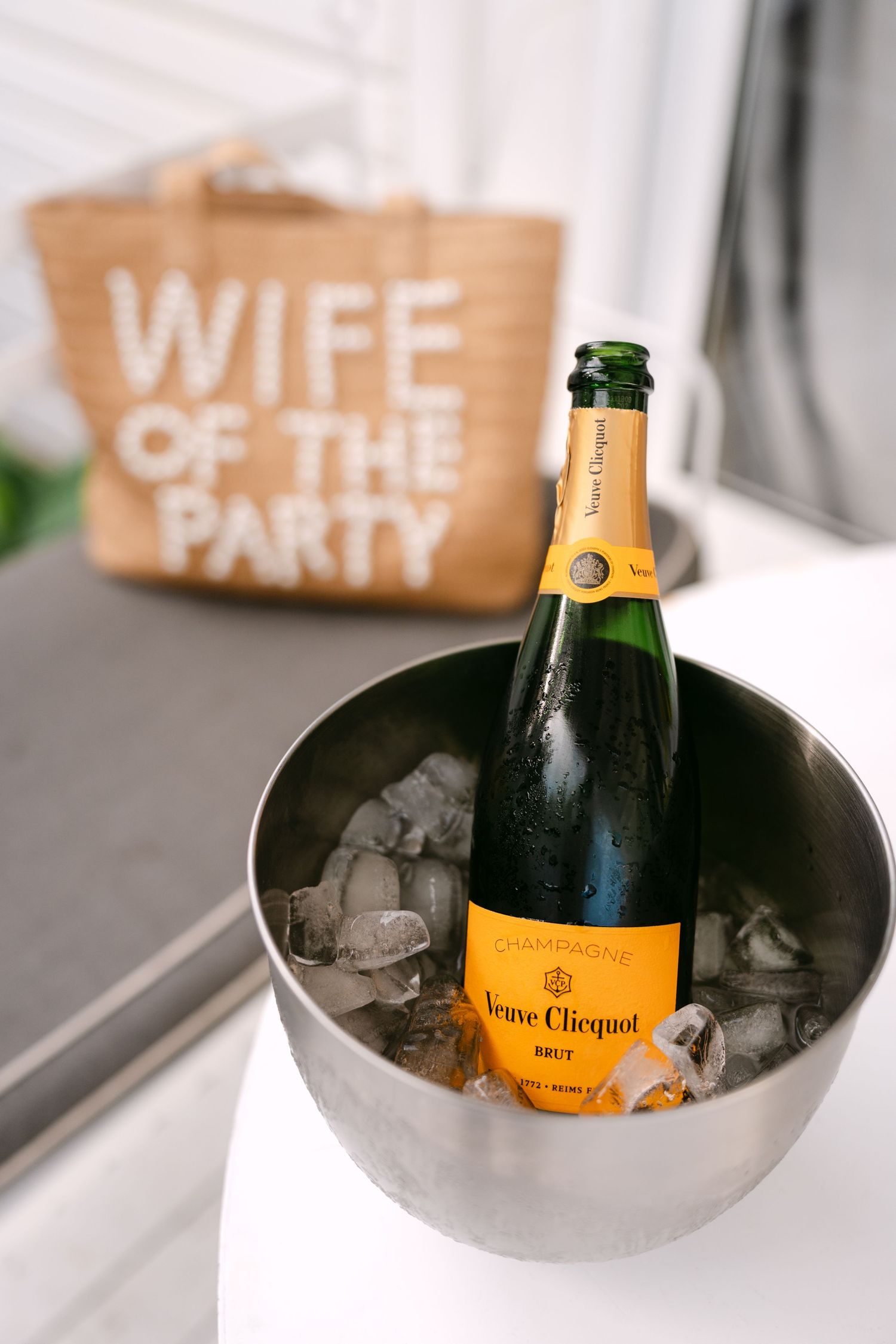Veuve Clicquot Brut champagne chilling in ice bucket with Wife of the Party tote bag in background.