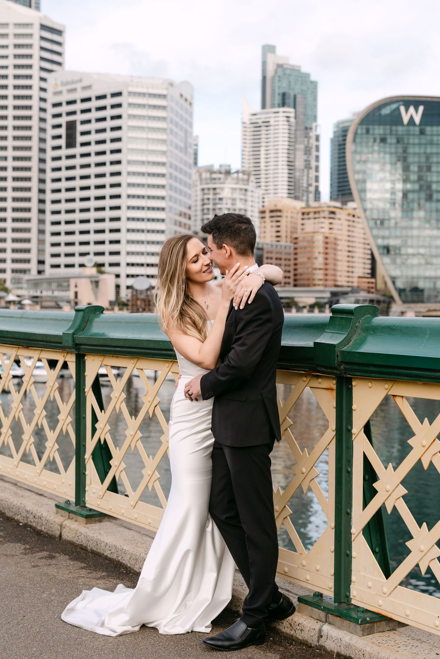 Bride and groom embracing on a bridge with Sydney city skyline and W Hotel in the background.