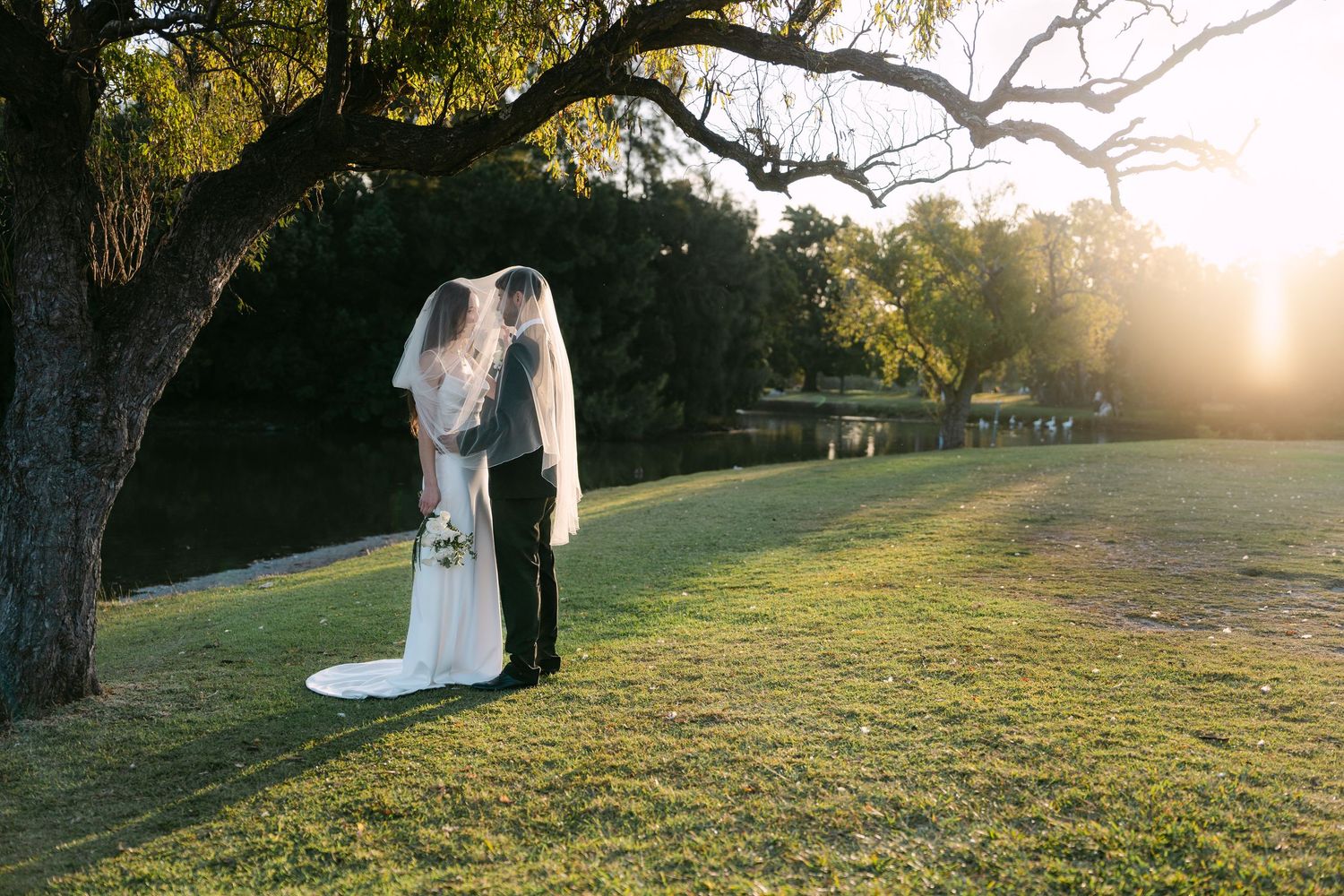 Bride and groom kissing under a large oak tree at sunset in Centennial Park
