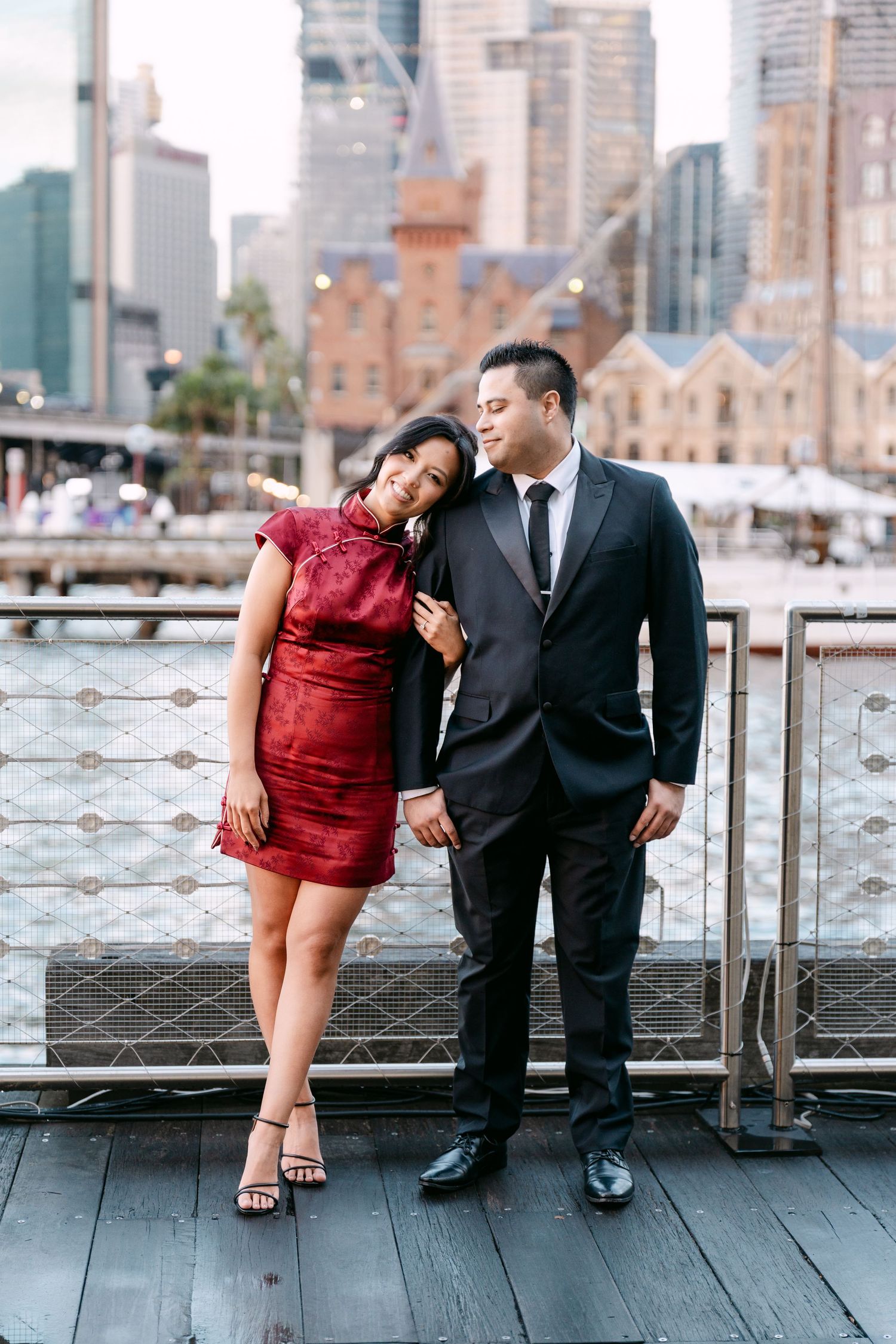 Pre-Wedding photos of Couple posing on waterfront deck with Sydney CBD skyline and Circular Quay in background.