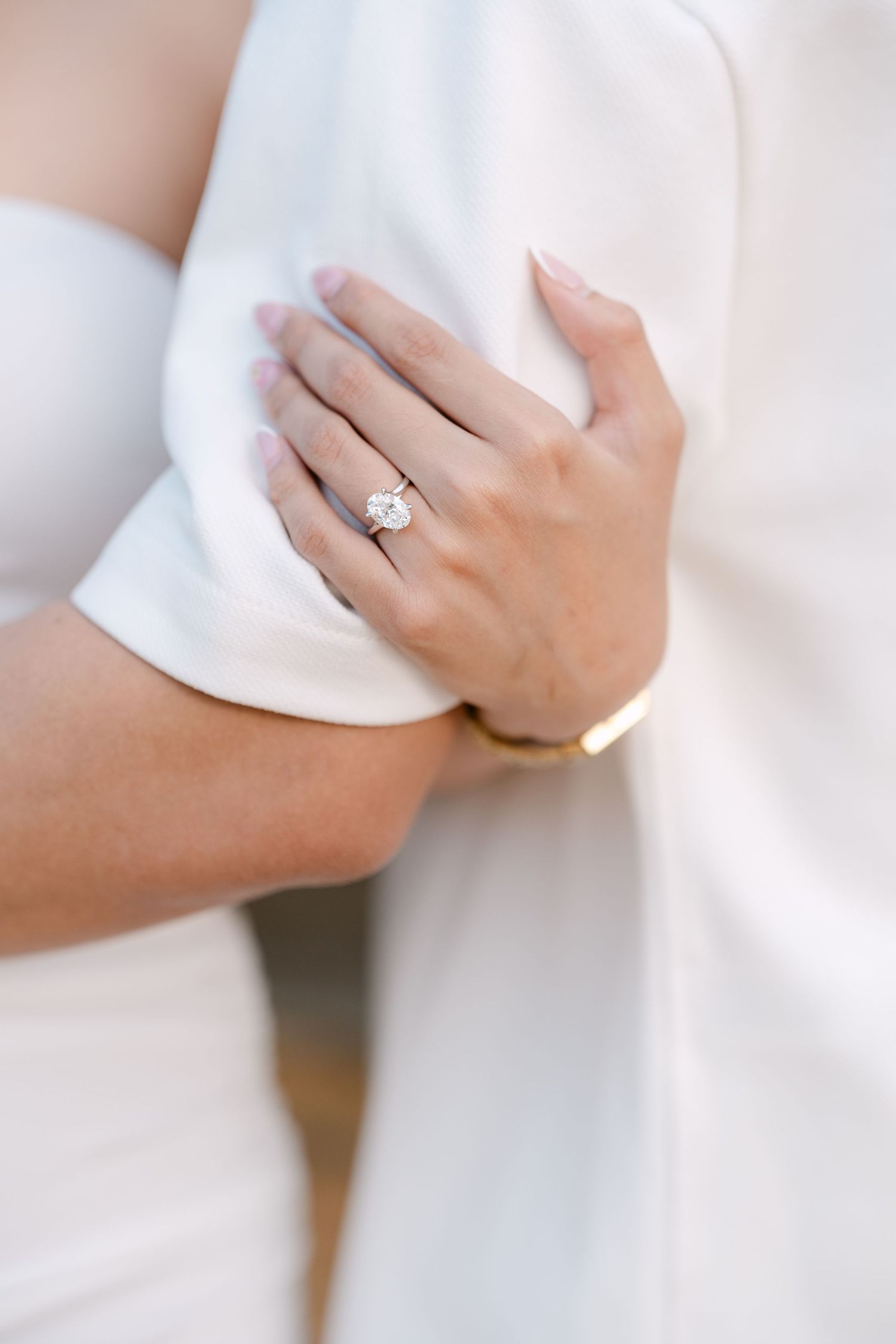 Close-up of elegant oval diamond engagement ring on bride's hand against white fabric.