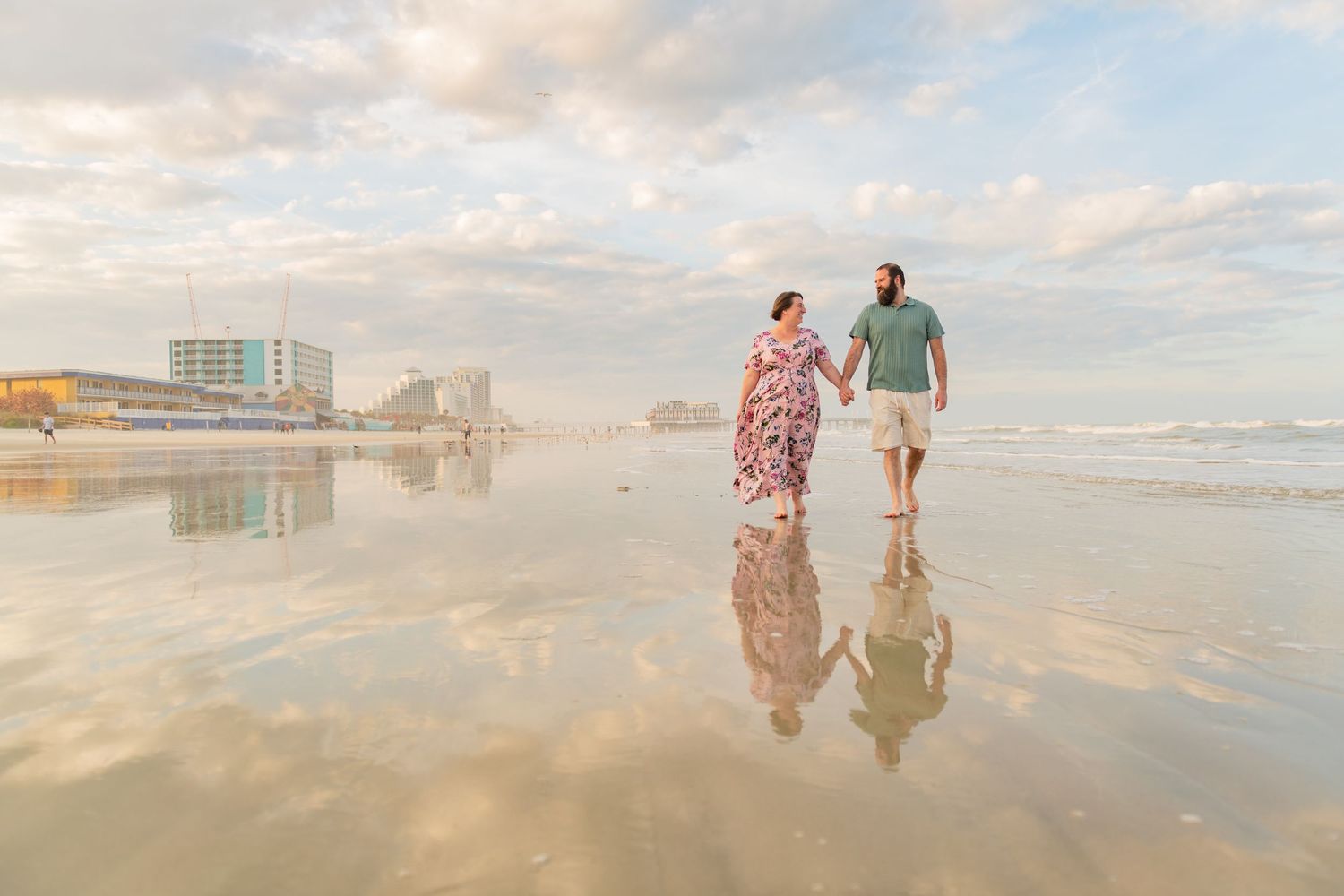 People walking along a reflective beach shoreline during a beautiful cloudy evening.