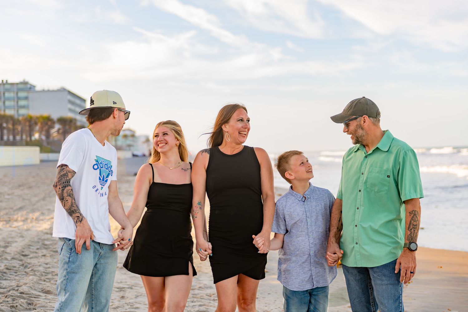 Family of five walking hand-in-hand on a sunny beach, smiling and enjoying a seaside vacation together.