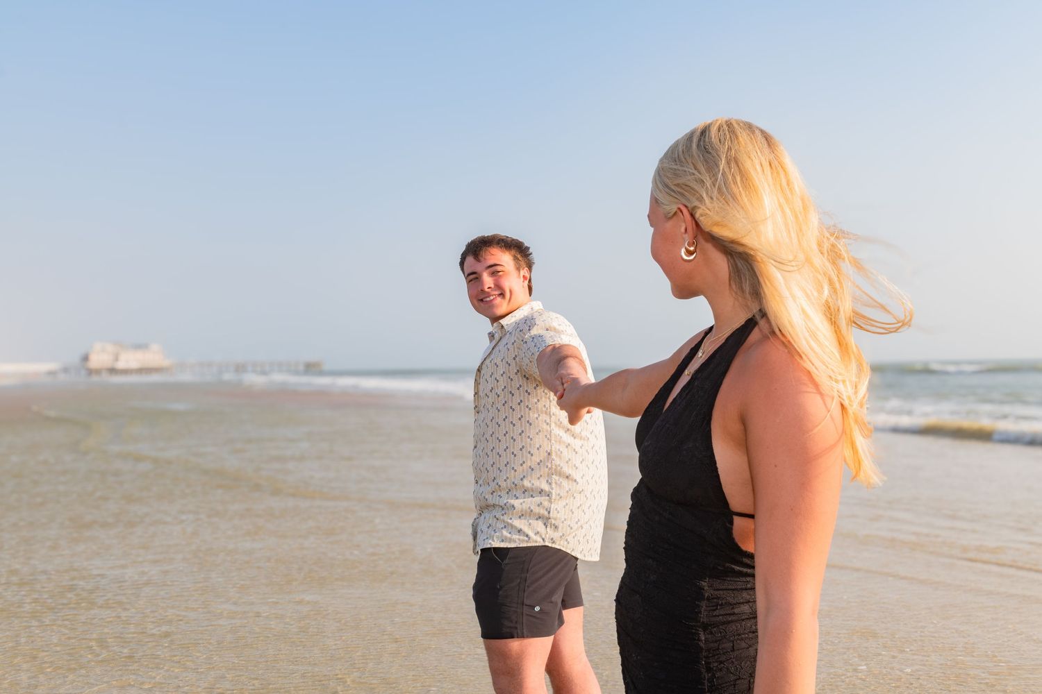 Couple holding hands and dancing on a sunny beach with ocean waves in the background.