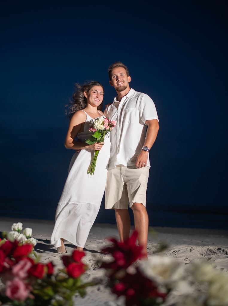 Romantic beach engagement photos with red flowers in the foreground.