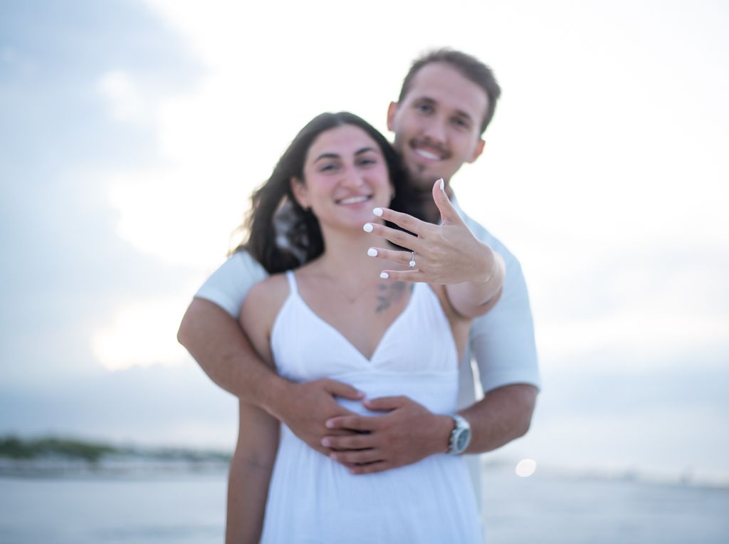 Couple embracing on a sunny beach in white outfits.