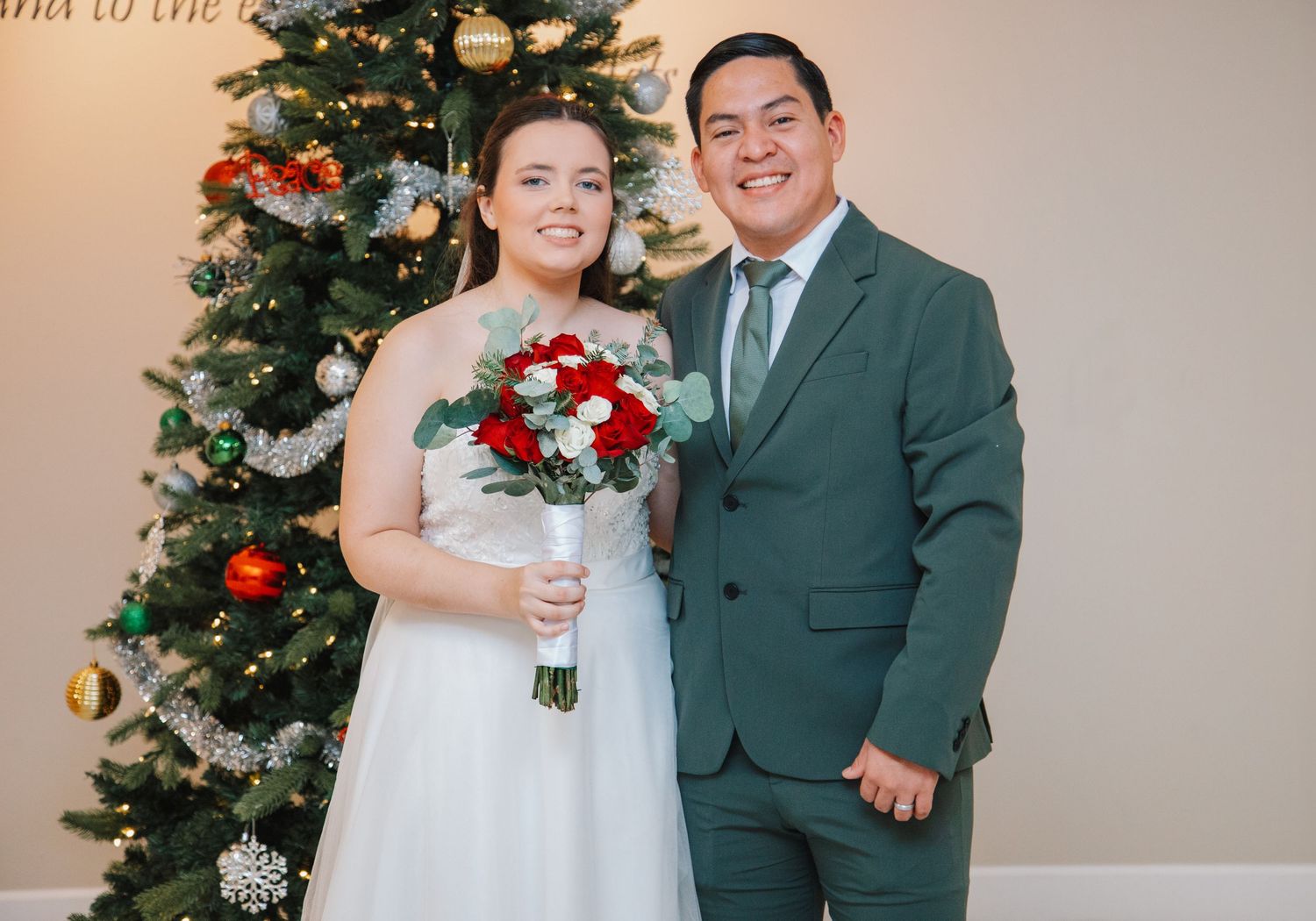 A festive holiday portrait in front of a decorated Christmas tree with red bouquet.