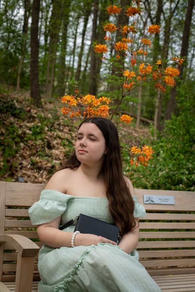A person in mint green dress sits on wooden bench with orange flowers blooming above.