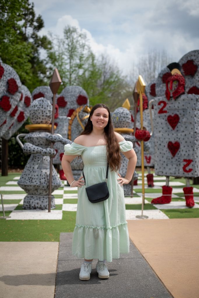Person in mint green dress posing near decorative wall with red heart patterns outdoors.