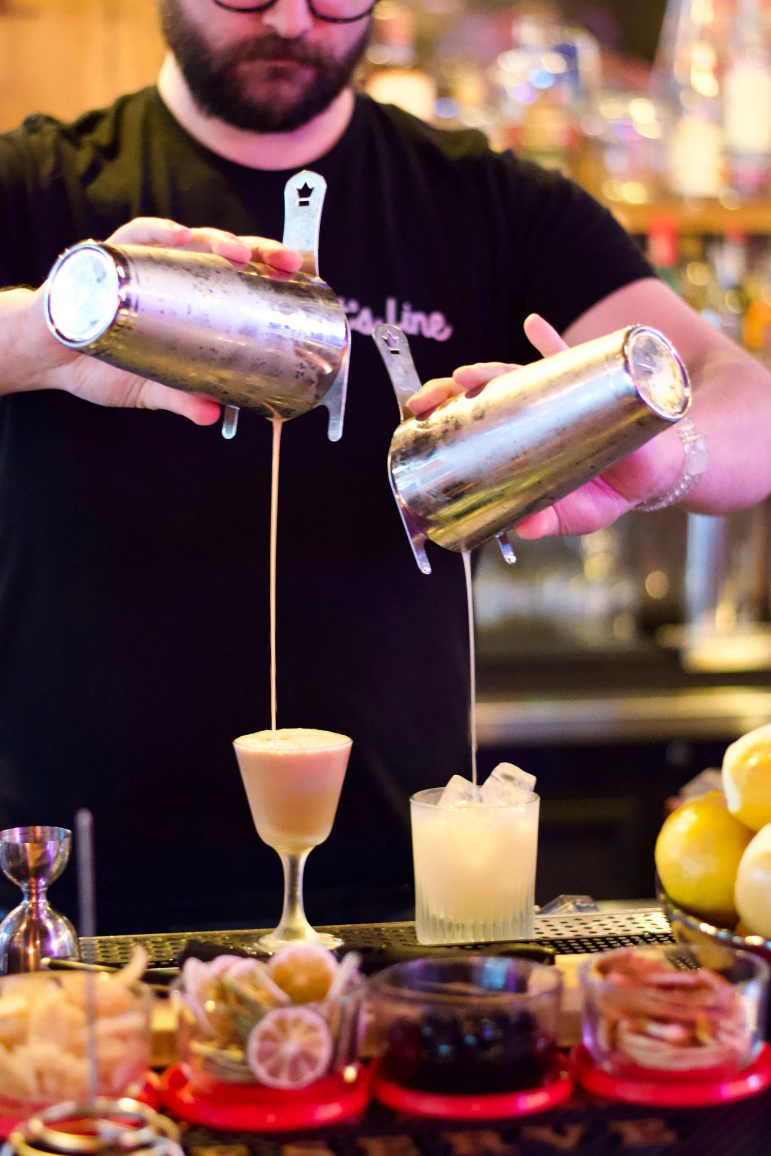 A bartender pouring a refreshing cocktail into a glass, with blurred bar shelves and neon lights creating an energetic atmosphere.