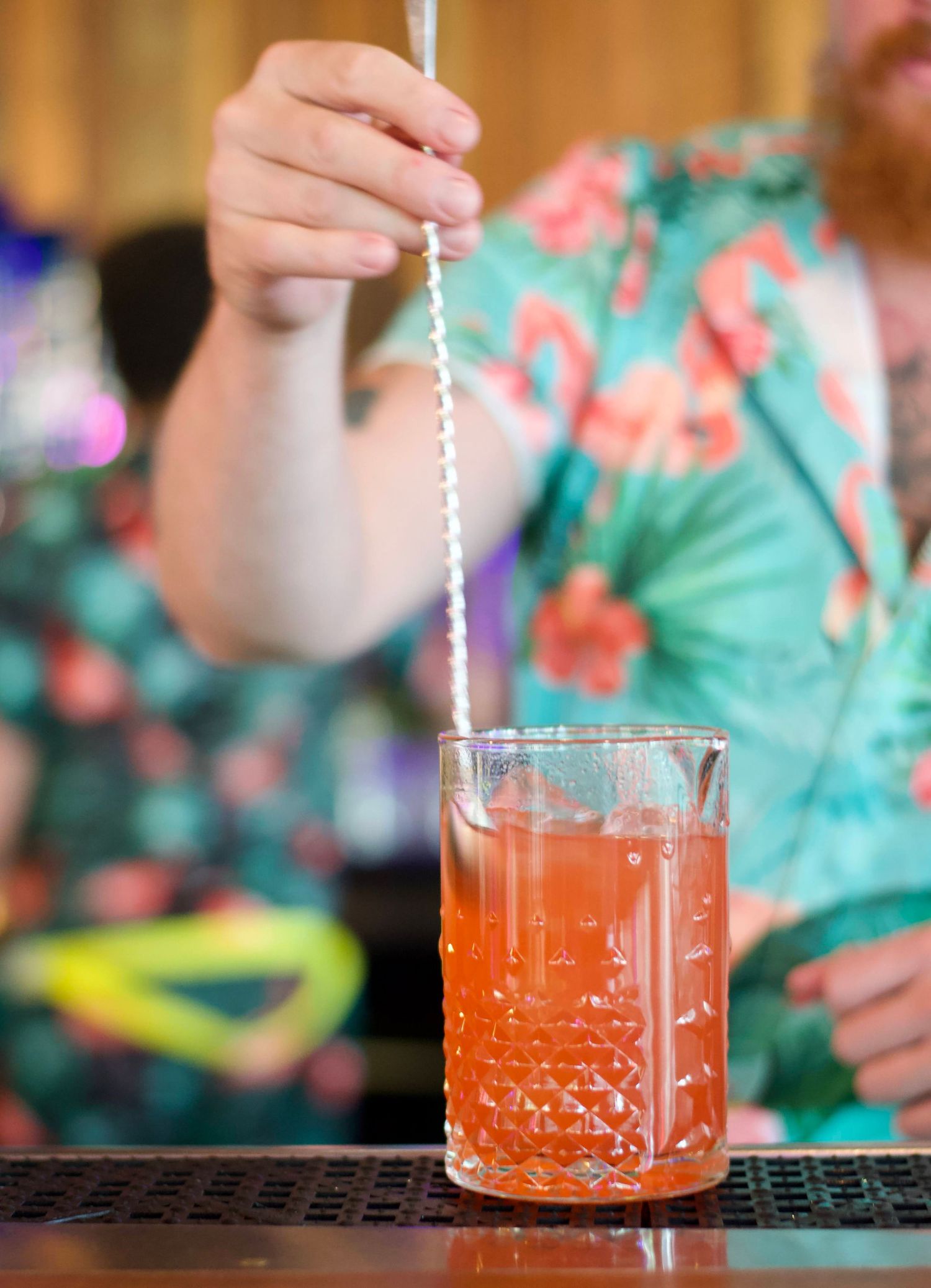 Close-up of a bartender’s hand pouring a drink into a glass, with vibrant garnishes adding a pop of color to the cocktail.