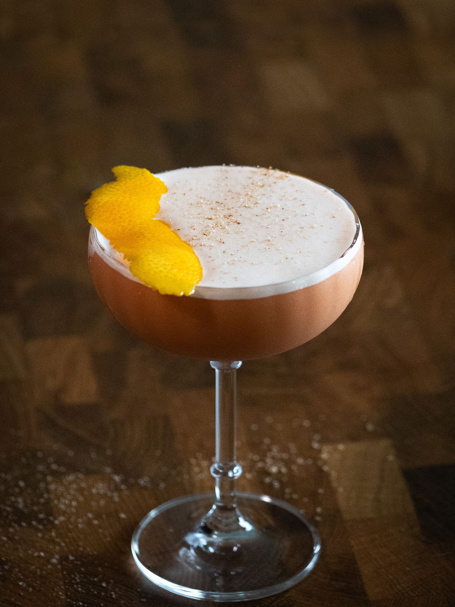 Crisp cocktail with a rim of salt, garnished with a lime wedge, sitting on a rustic bar counter with natural lighting highlighting its detai