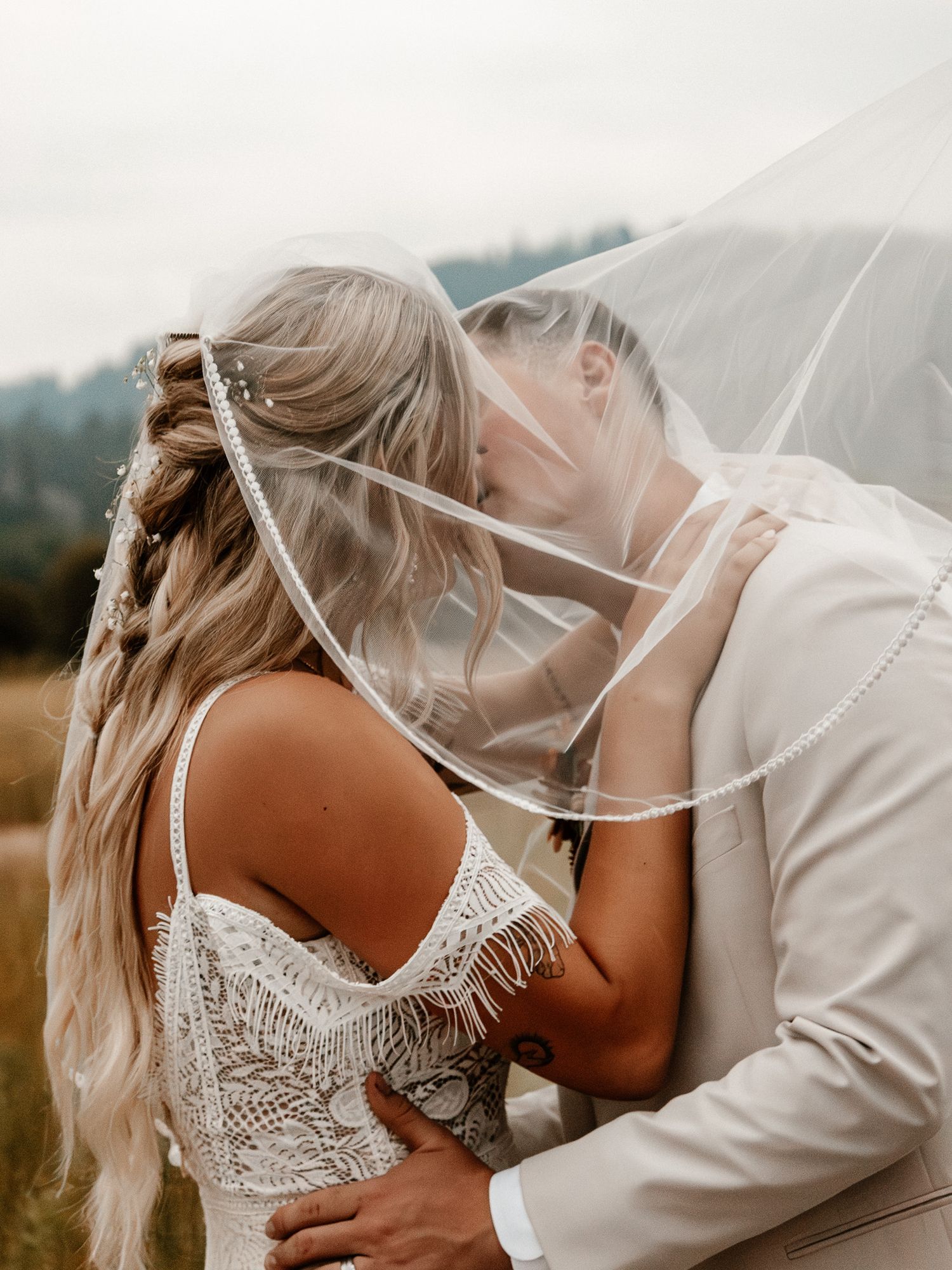 A couple embraces during an elopement, the brides veil shrouding them both in a dreamy way.