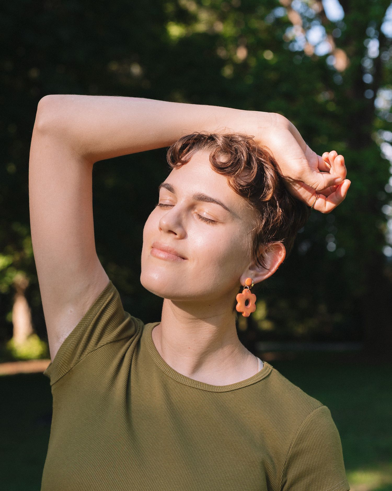 High fashion model in an elegant pose outdoors, surrounded by nature’s beauty, with soft, natural light illuminating the scene