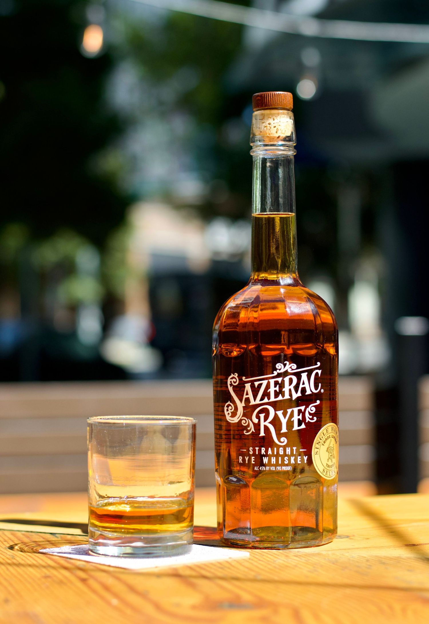 A bottle of premium whiskey with a glass filled with ice, artfully arranged on a wooden bar top with warm lighting.