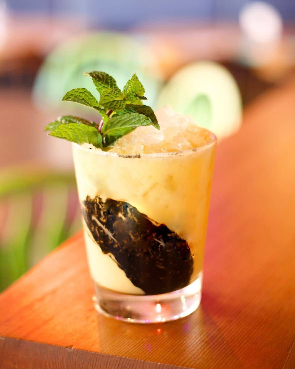 A chilled cocktail with condensation on the glass, elegantly displayed on a bar top, with a backdrop of blurred bar shelves.