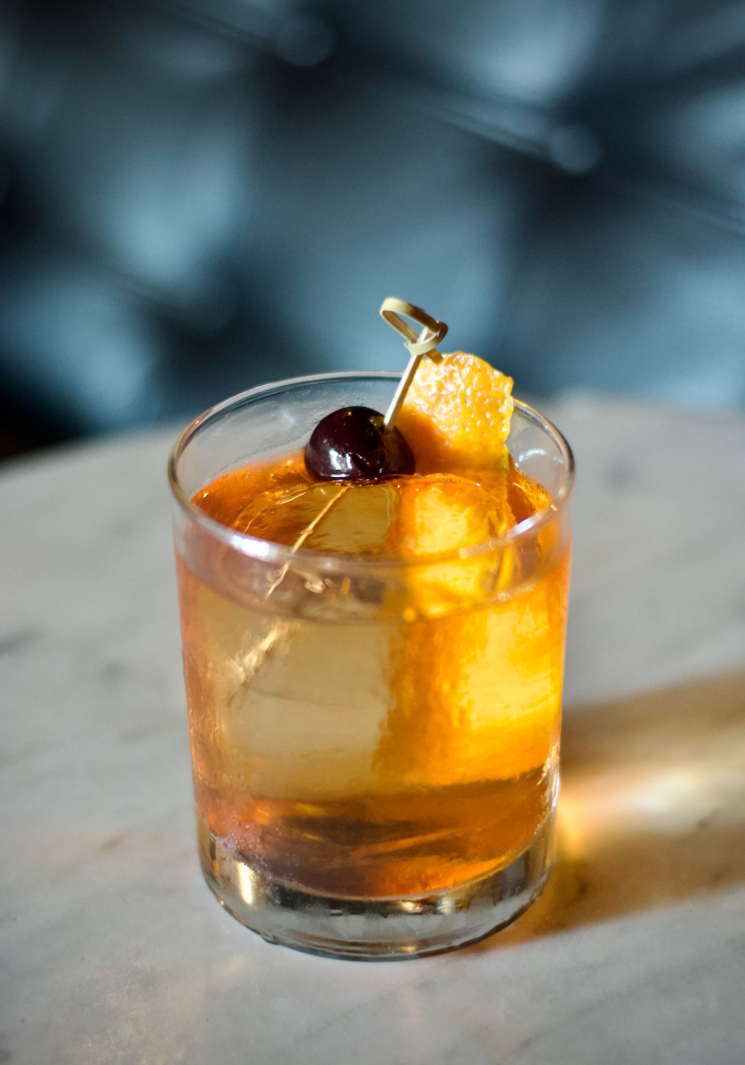 lose-up of a sparkling cocktail in a crystal glass, garnished with a slice of lime and mint leaves, set against a blurred bar backdrop