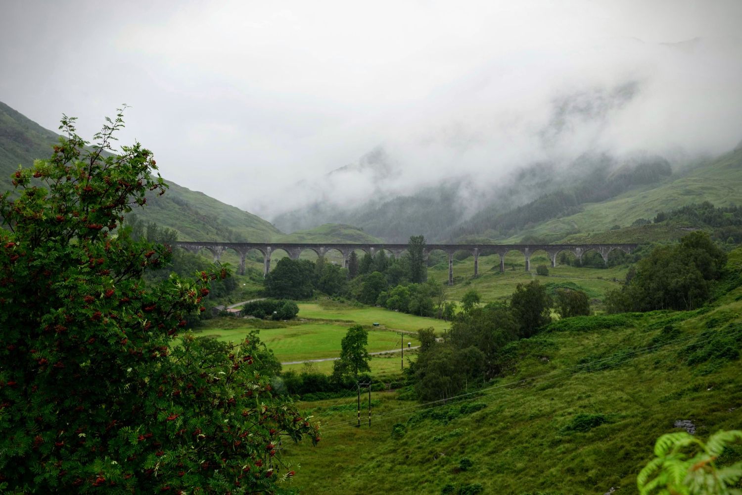 Mist-covered Scottish mountains, with rolling hills and a serene loch reflecting the cloudy skies