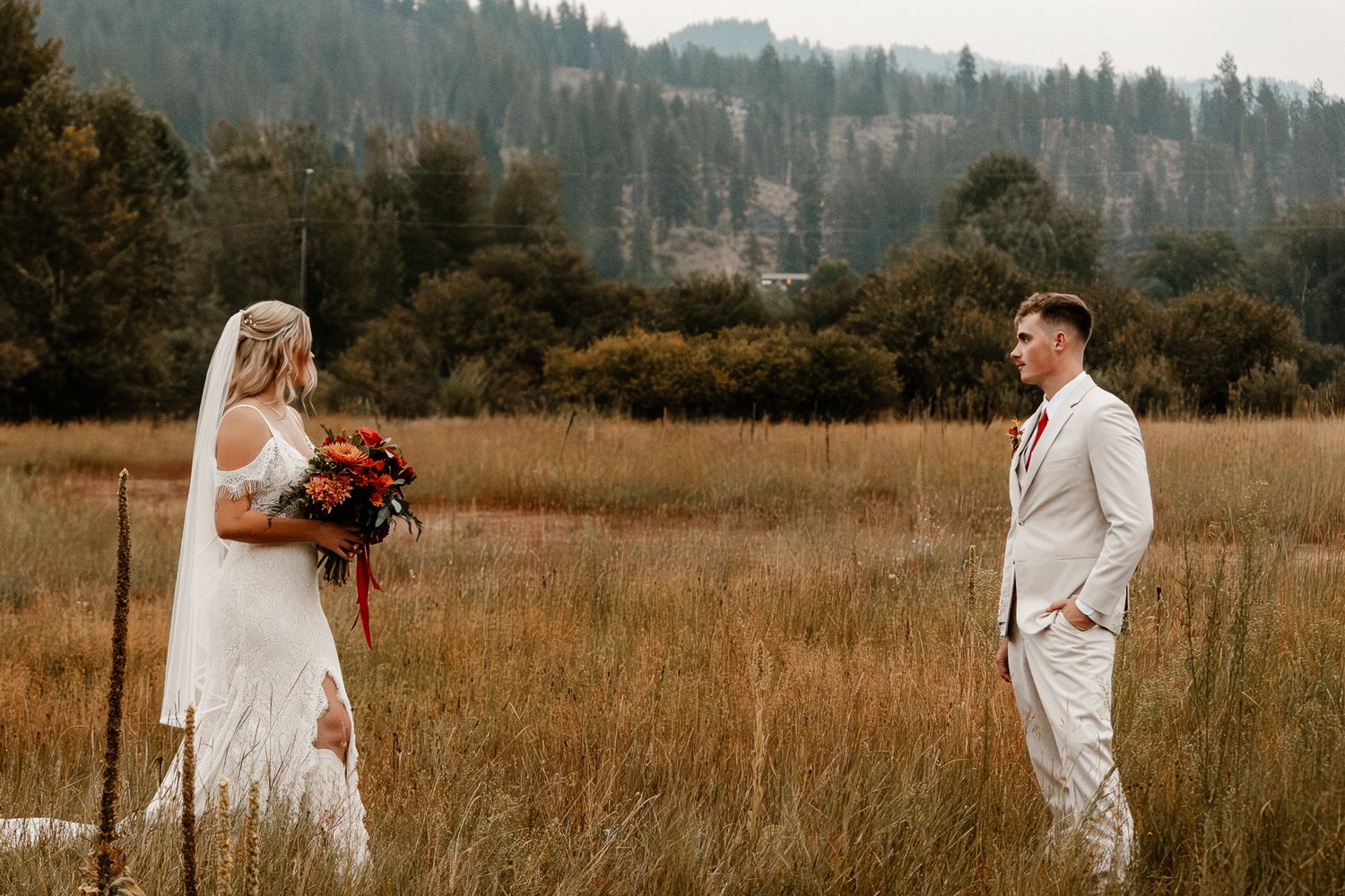 Couple sitting close together on a grassy hilltop, gazing into each other’s eyes as the sun sets behind them.