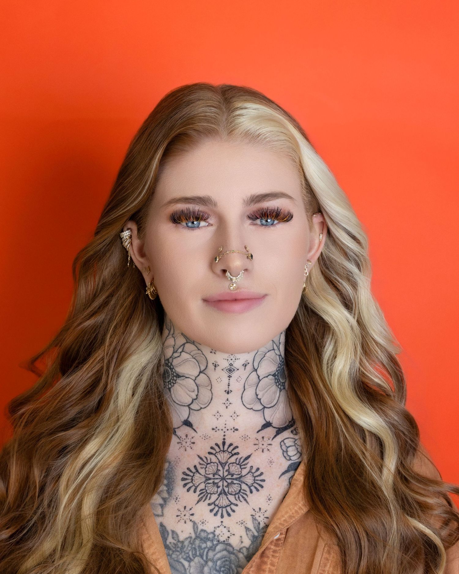 A heavily pierced and tattooed model smiles at the camera during a high fashion photoshoot.