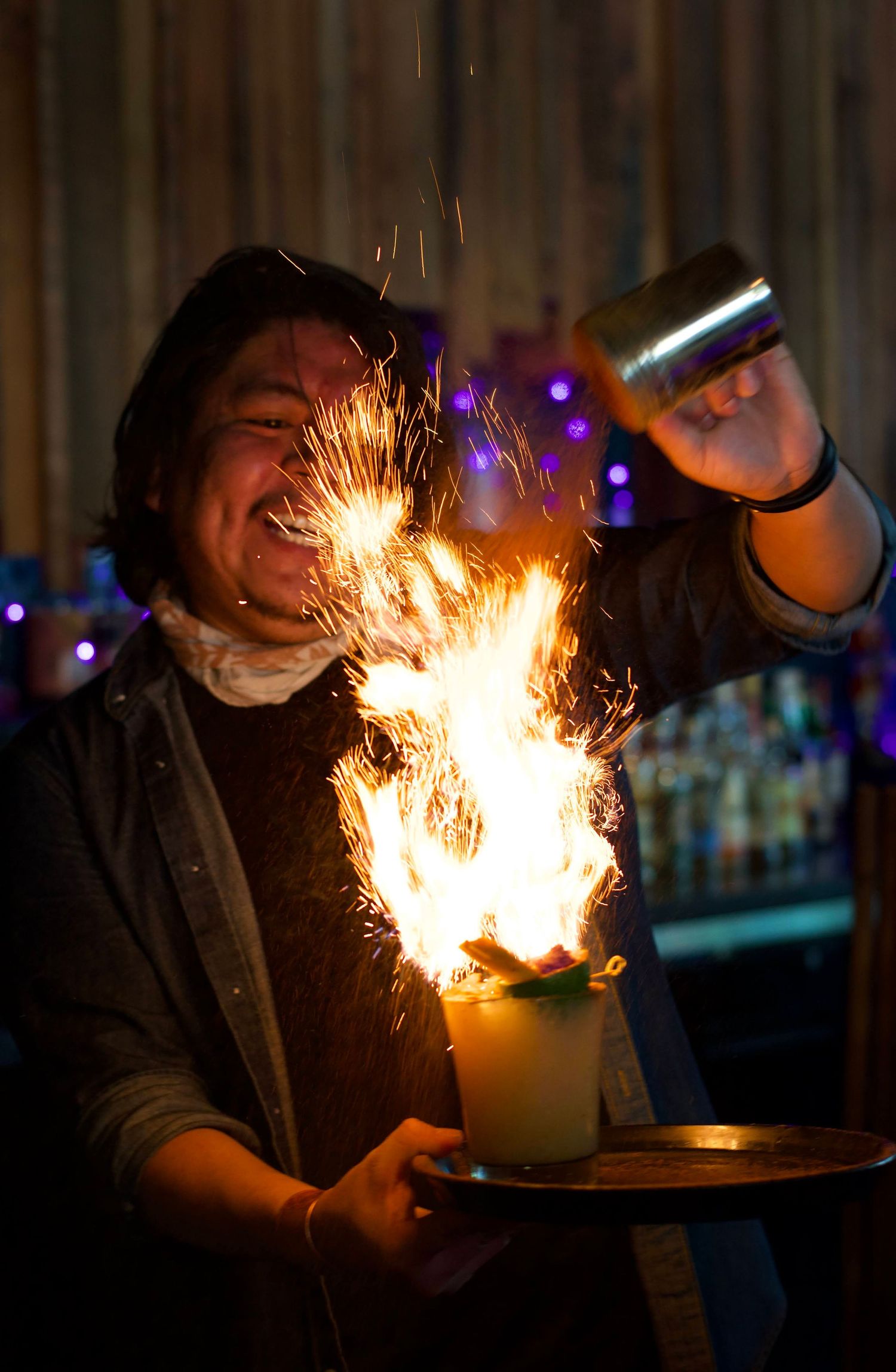 Bartender smiling and serving a refreshing drink to a customer, with warm, ambient lighting highlighting the bar’s rustic charm.