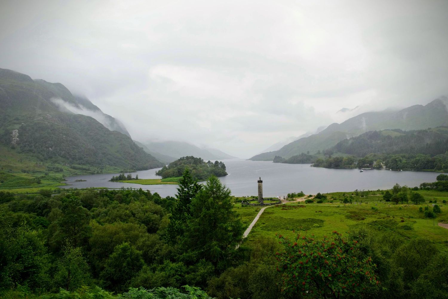 Wide-angle shot of the iconic Scottish lochs, with calm waters reflecting the towering mountains and dramatic skies.