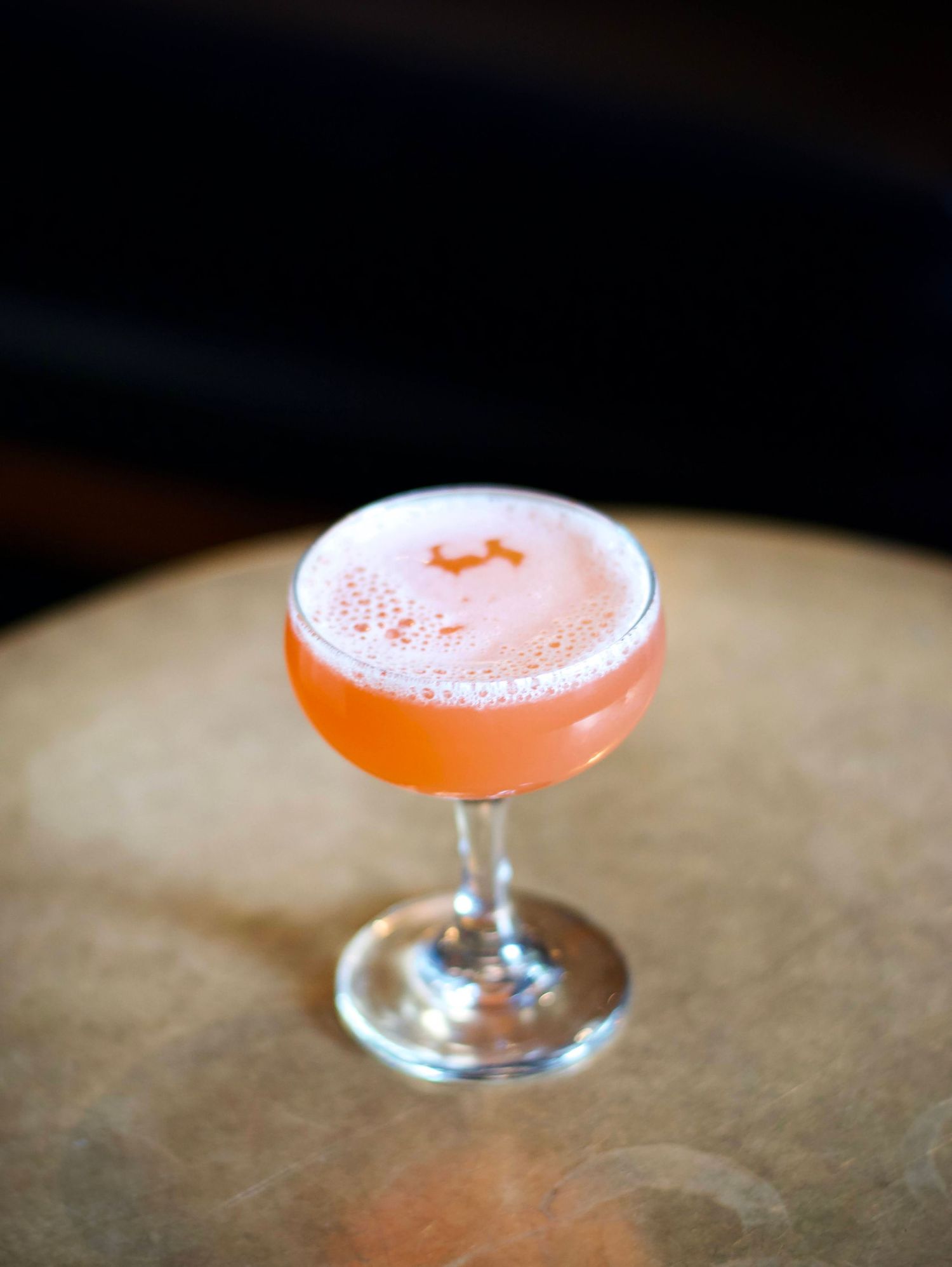 ignature cocktail with a vibrant, layered presentation, resting on a wooden bar counter with fresh fruits and herbs around it