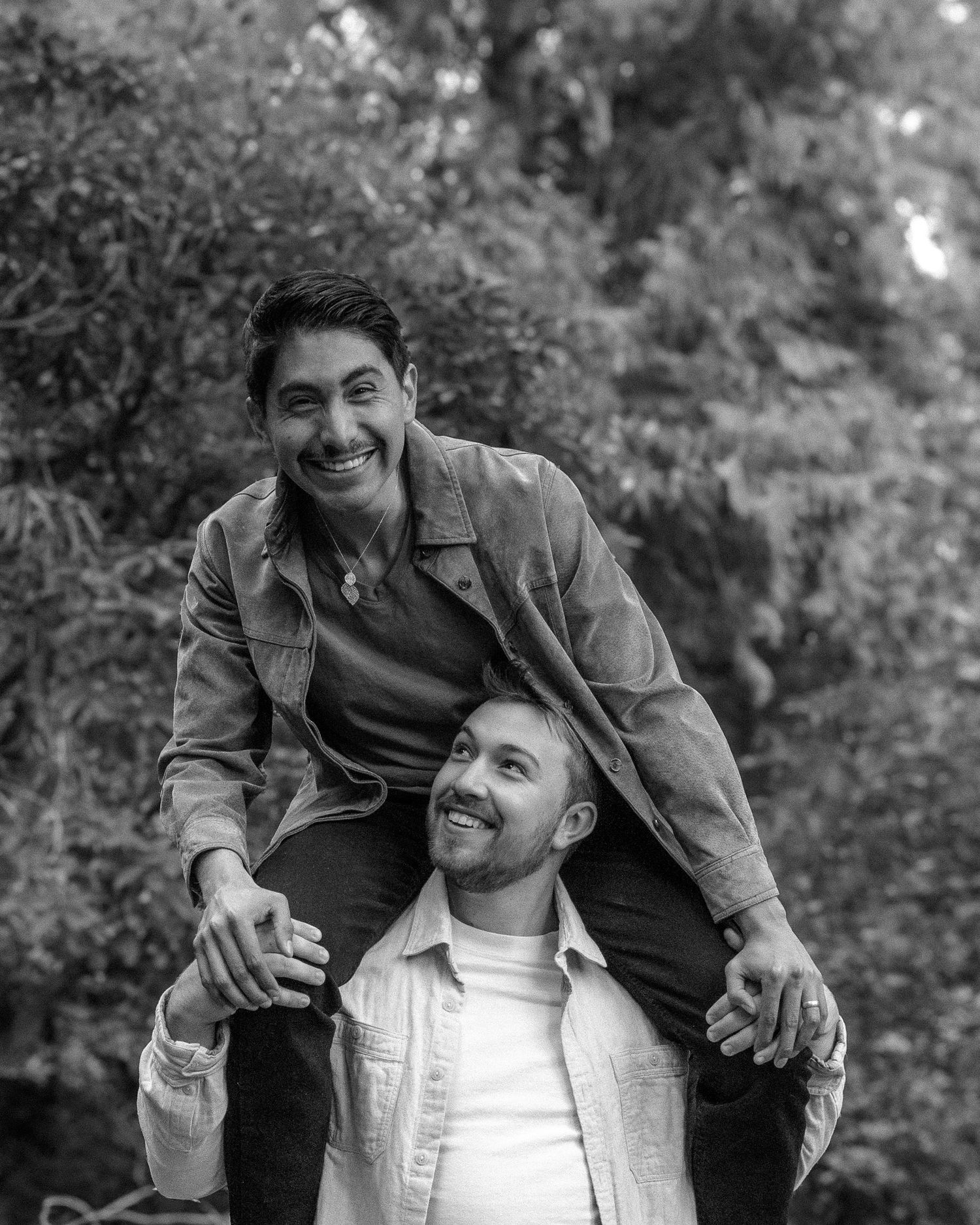 Outdoor photoshoot of a couple laughing together by a creek, with natural rocks and greenery adding to the serene atmosphere.