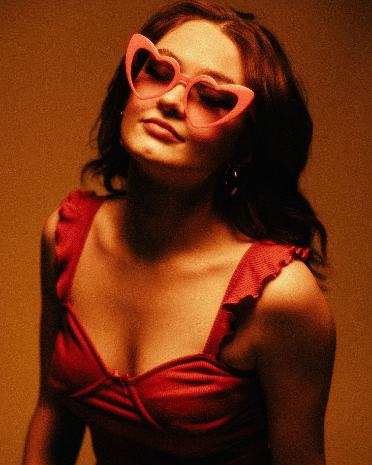 Stylish portrait in warm tones featuring heart-shaped pink sunglasses and a red ruffled dress.