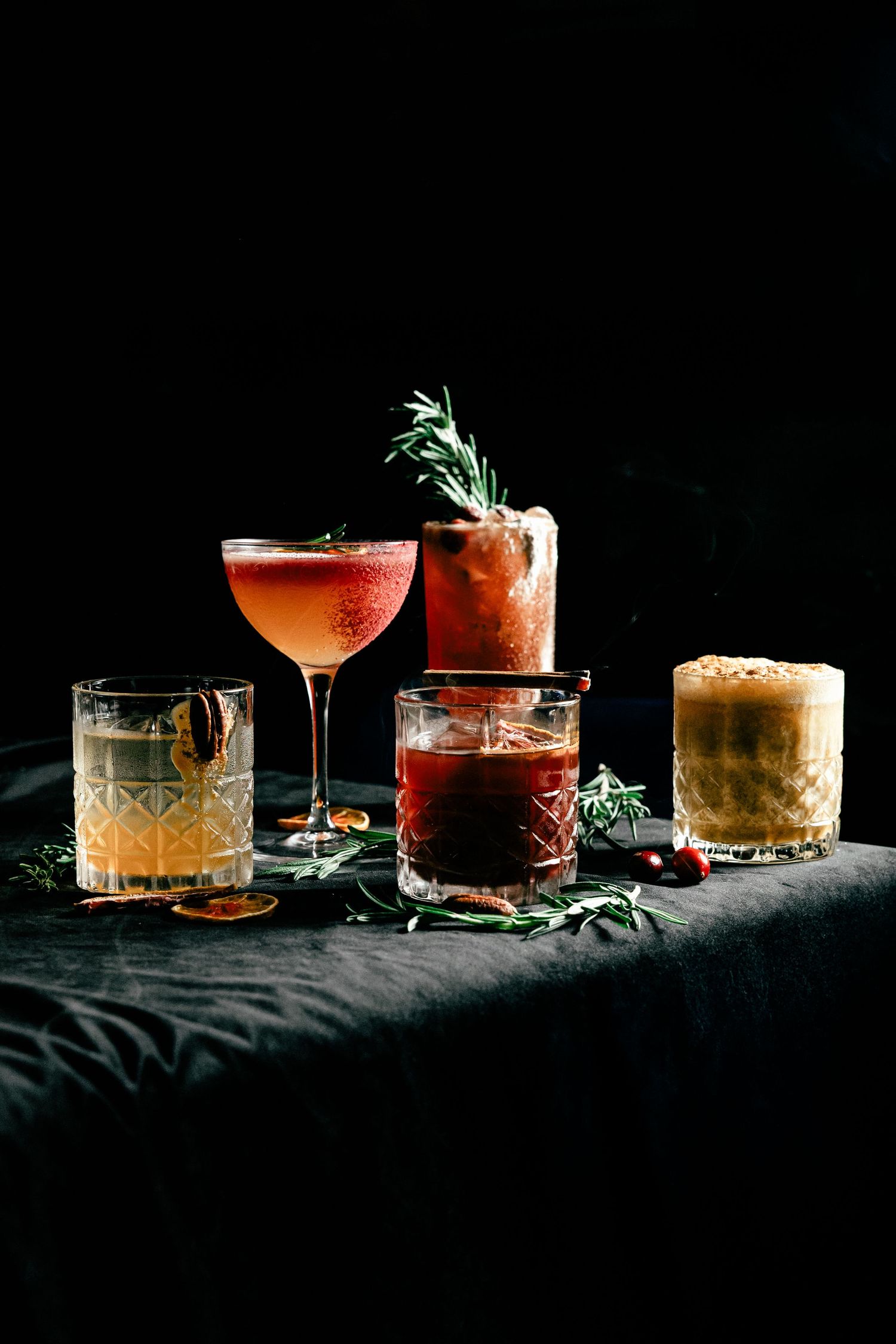 Collection of elegant cocktails with herb garnishes displayed on dark fabric.