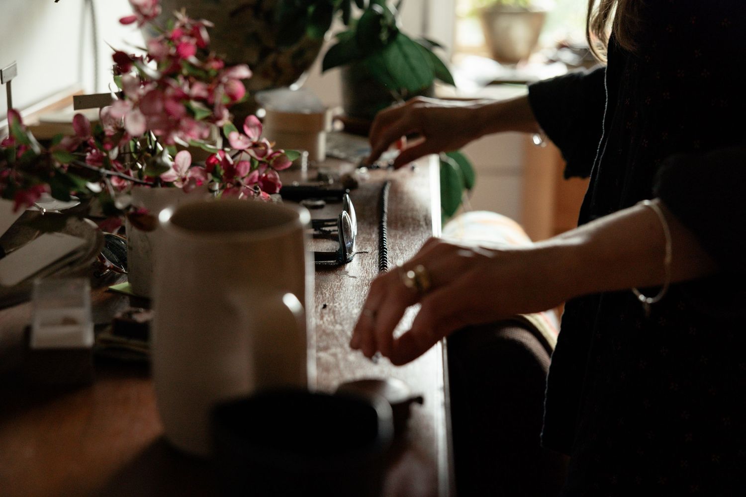 Hands preparing drinks on a counter decorated with pink flowers in soft natural lighting.