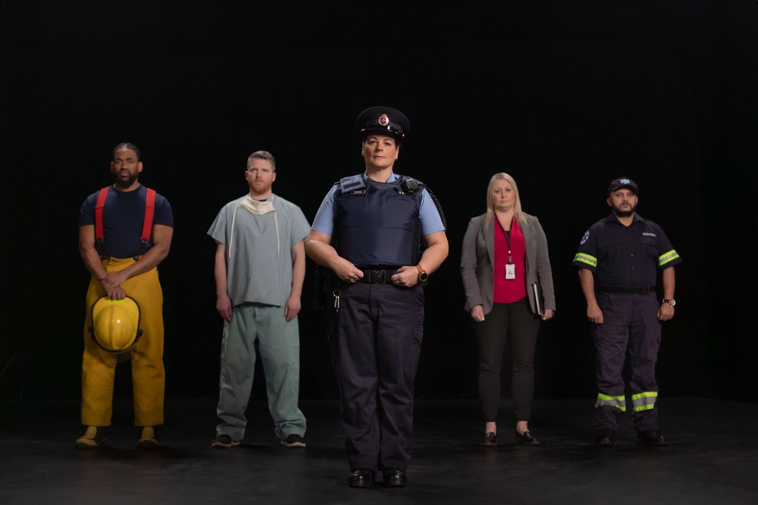 Group of emergency workers and essential personnel standing in a row against a black background.