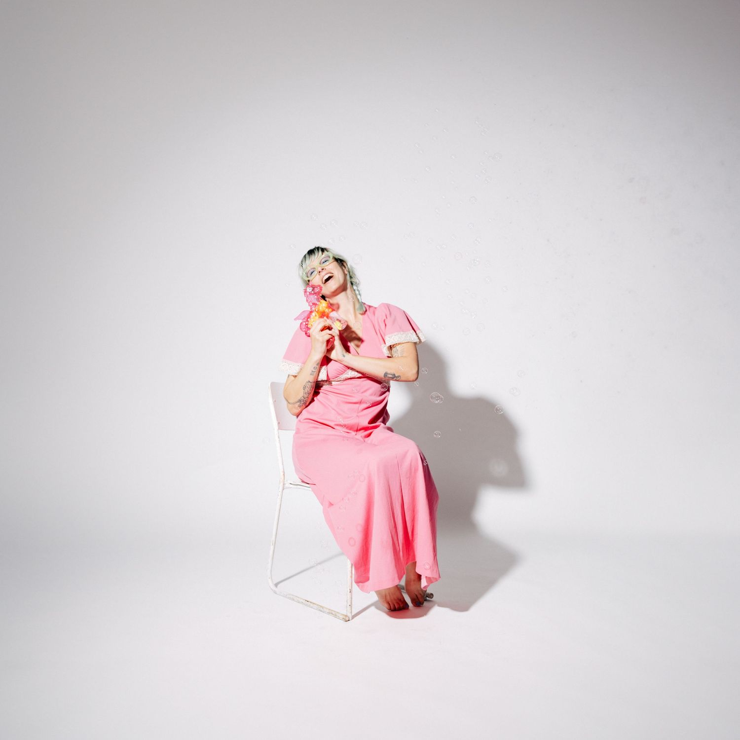 Figure in a flowing pink dress poses against a white background in a dynamic studio photoshoot series.