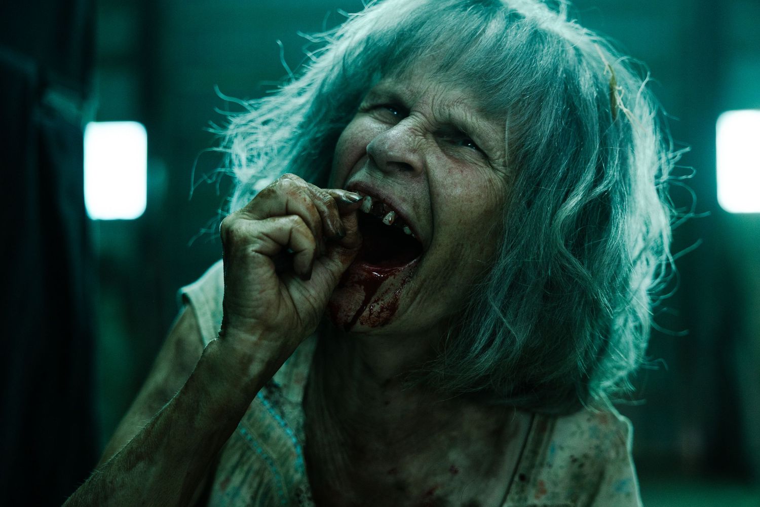 A figure with messy pale hair screams into a microphone under green lighting in a dark moody setting.