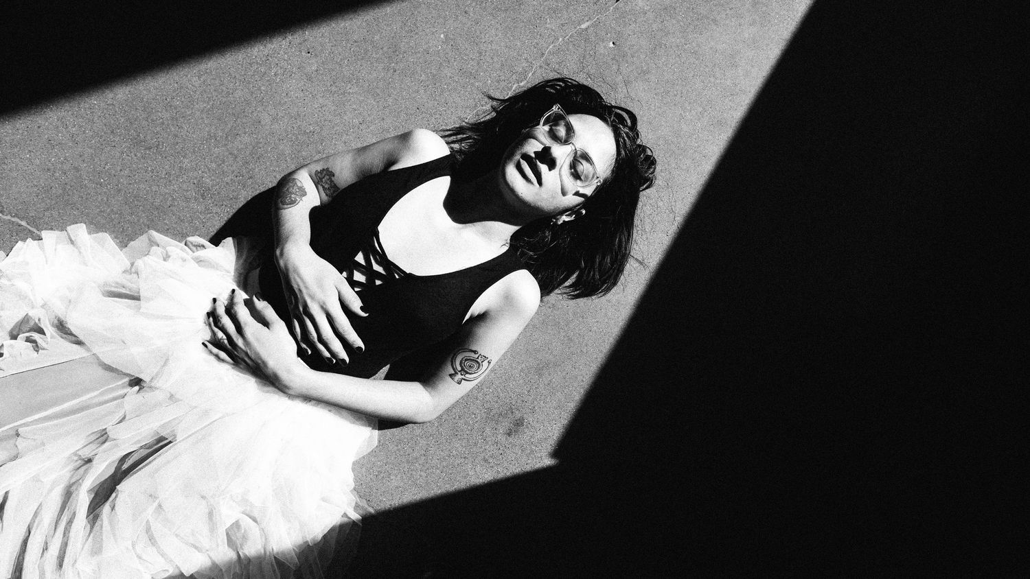 A dramatic black and white photograph showing a dancer in a flowing white tulle skirt posed under a spotlight.