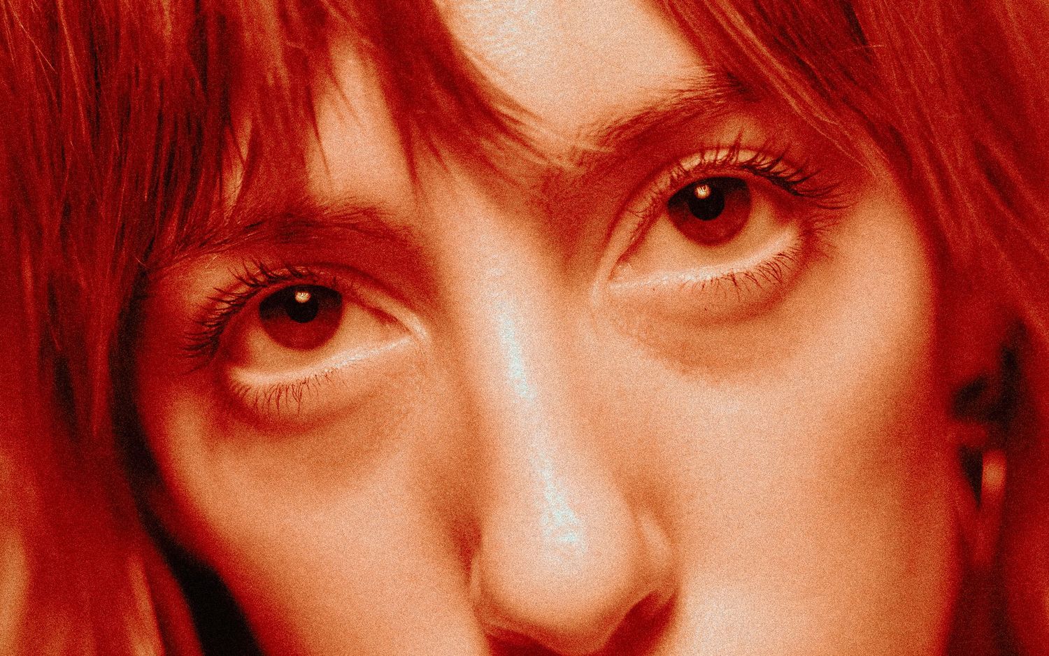 Close-up portrait with intense red-tinted lighting showing striking red eyes and matching red hair.