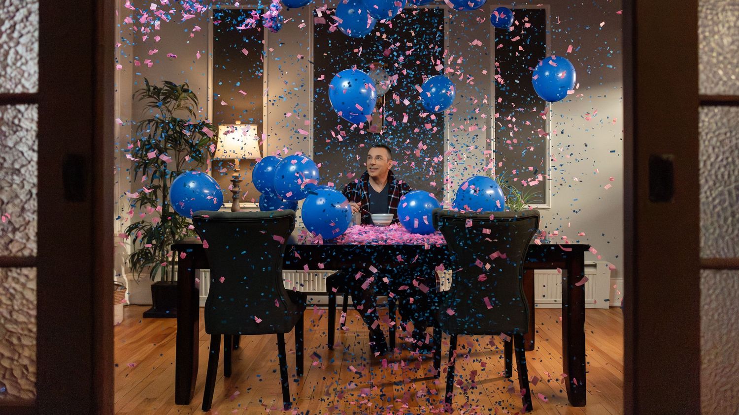 Teal balloons and confetti fill the air in a large room with decorative lighting and architectural details.
