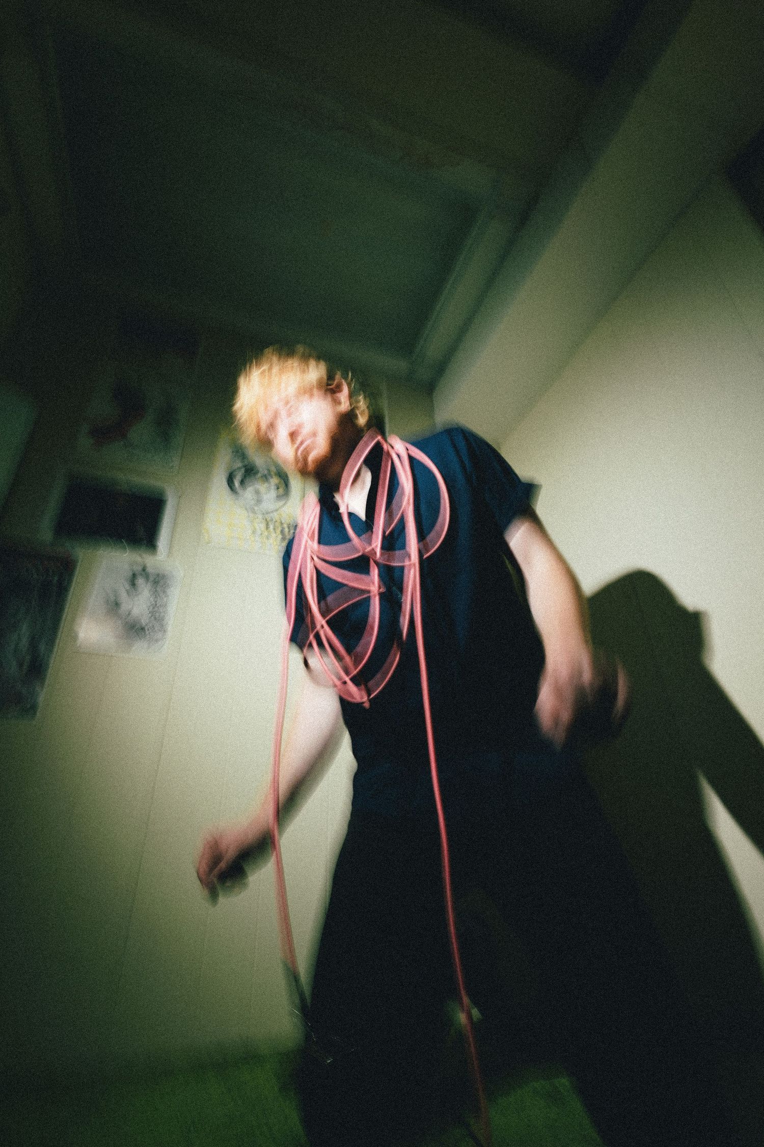 A blurred motion photo taken in dark lighting shows someone wearing black with pink cords in an indoor setting.