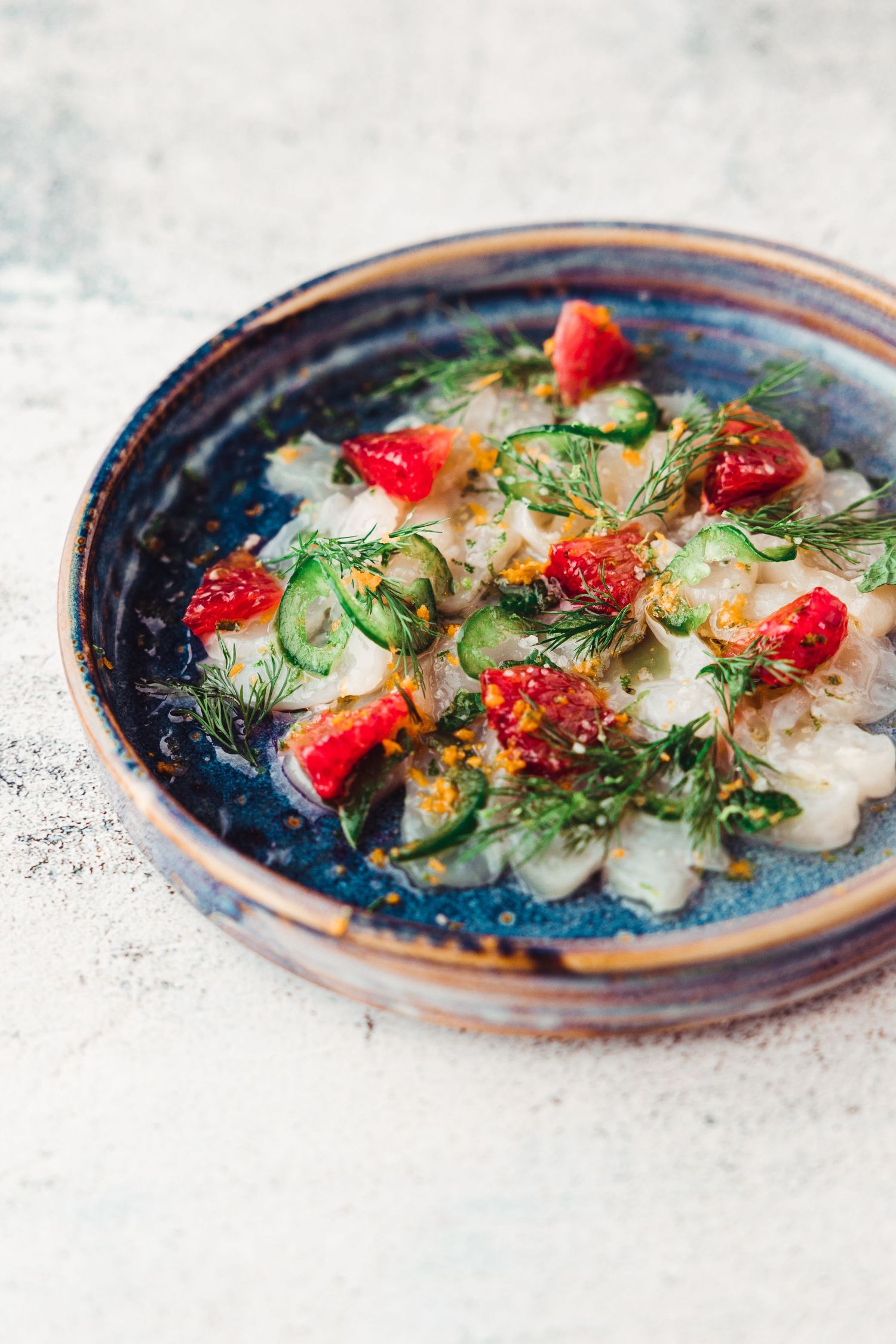 Fresh crudo or carpaccio with cherry tomatoes and herbs served on a rustic blue ceramic plate.