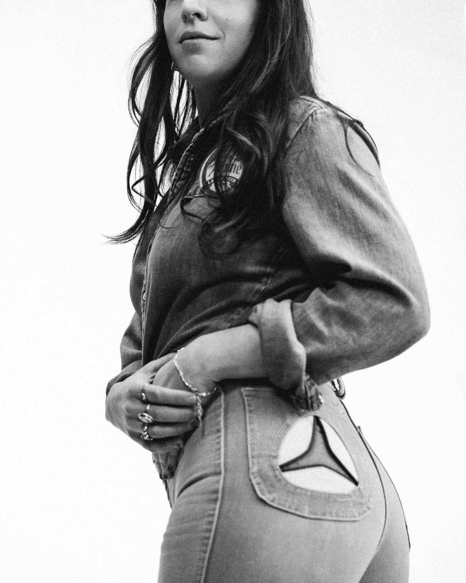 Black and white fashion photograph showing a woman in denim jeans and jacket posing from the side.