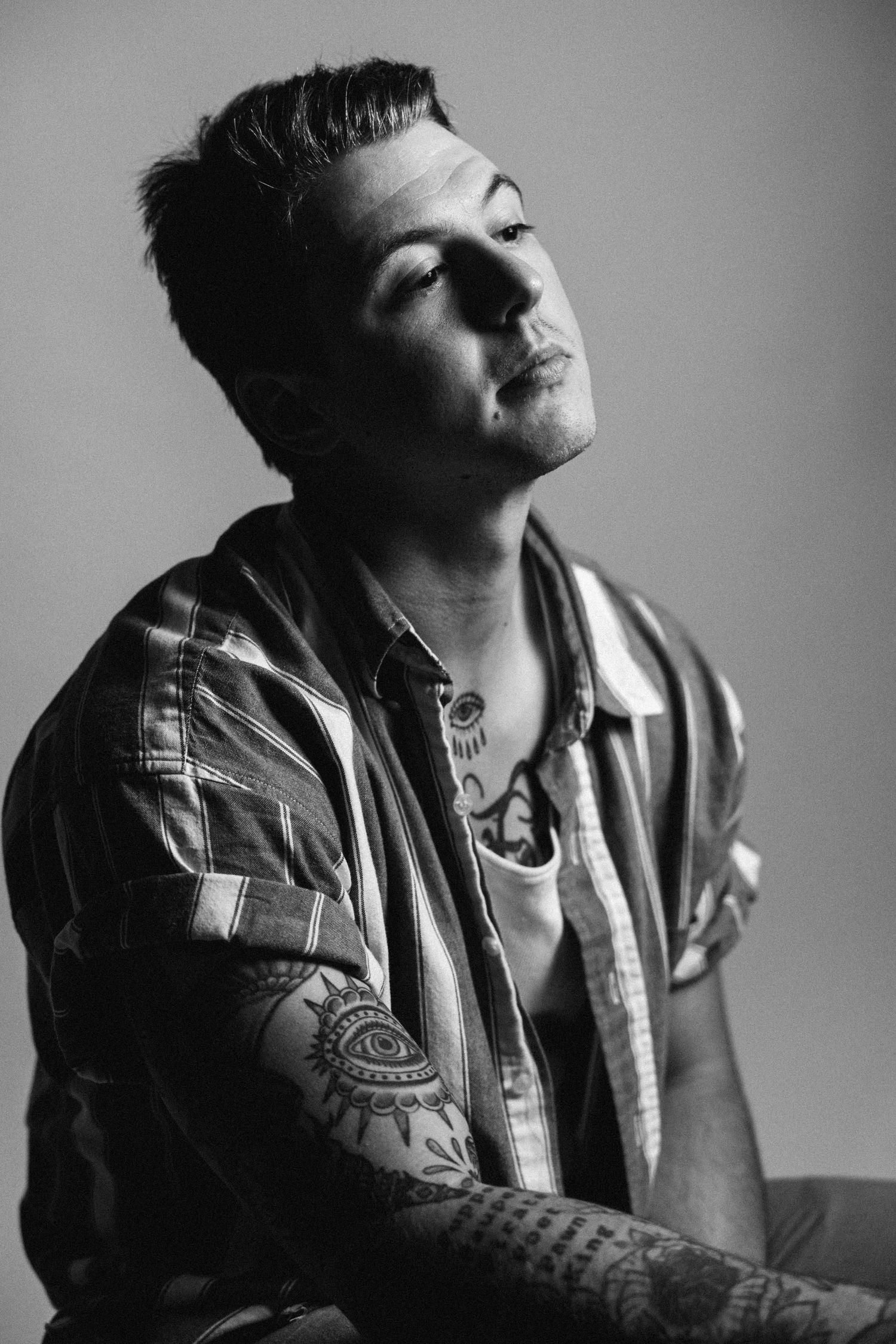 Black and white photo series showing a person in denim jacket with tattoos tilting their head against a gray backdrop.