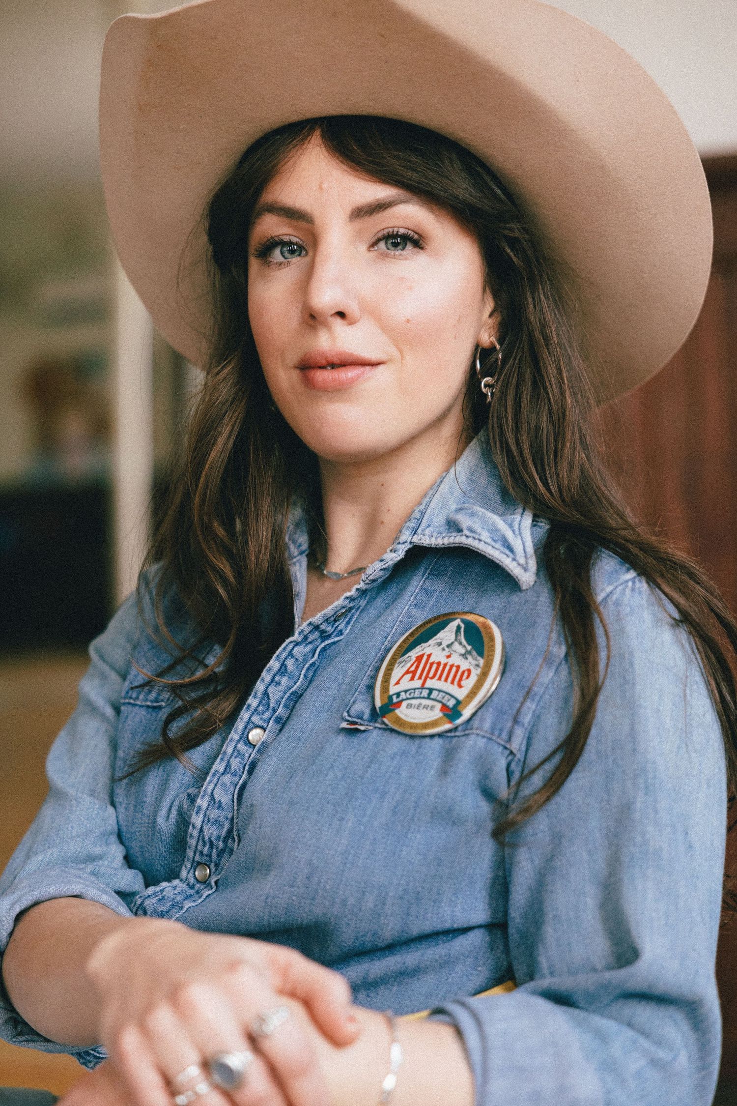 A person wearing a denim shirt and beige cowboy hat sits casually in a western-inspired portrait.