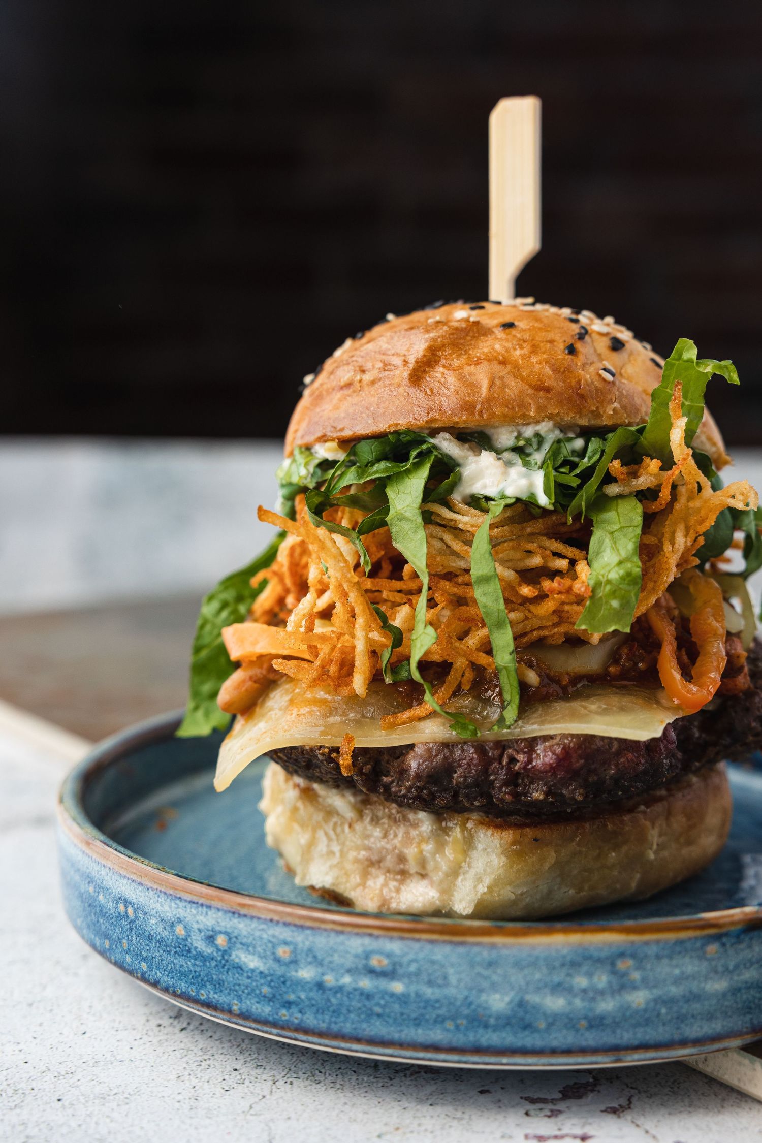 Gourmet burger with melted cheese, crispy fried onions and fresh greens served on a blue ceramic plate.