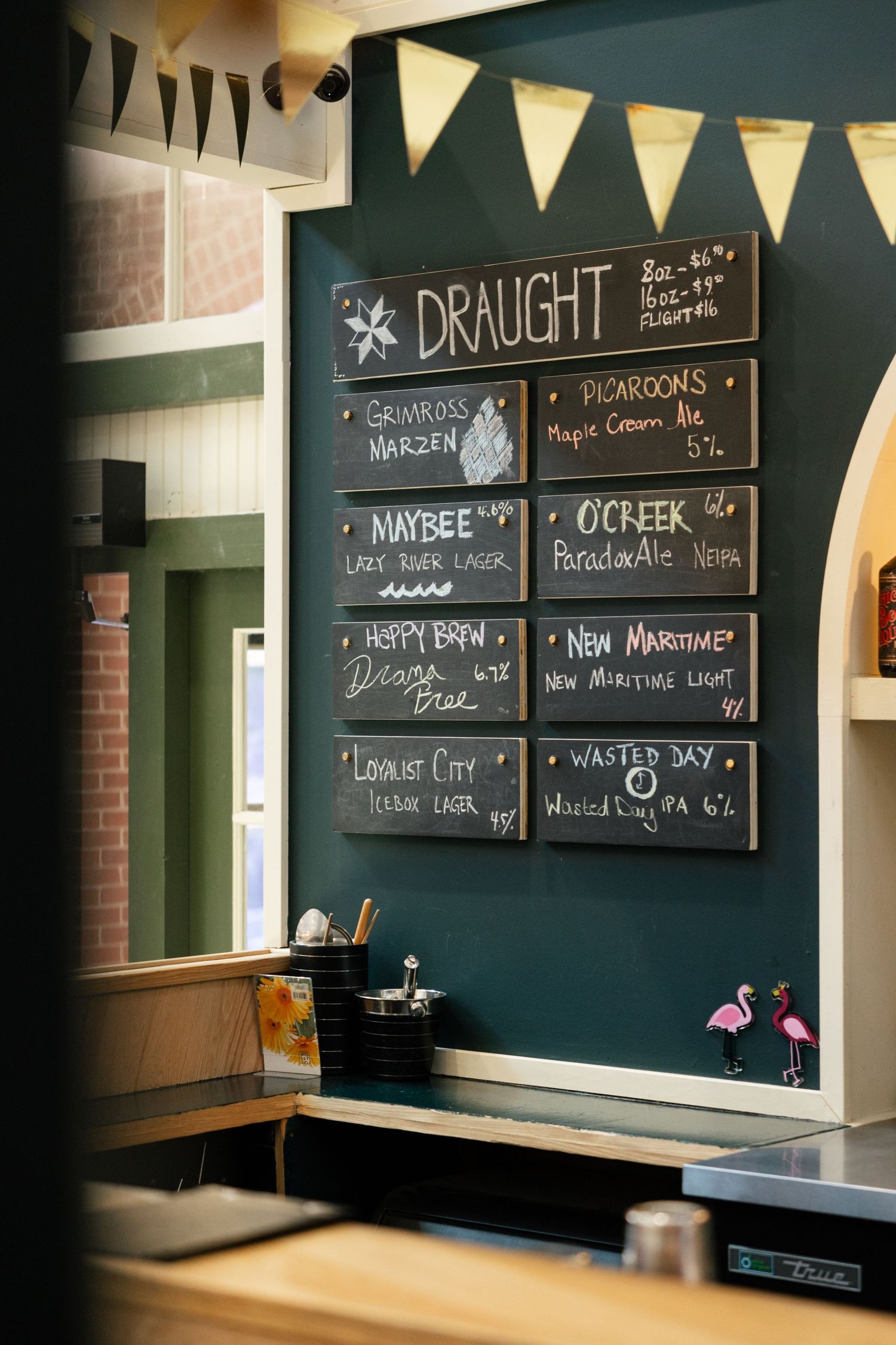 A chalkboard menu displays craft beer options with decorative bunting flags above in a cozy pub setting.