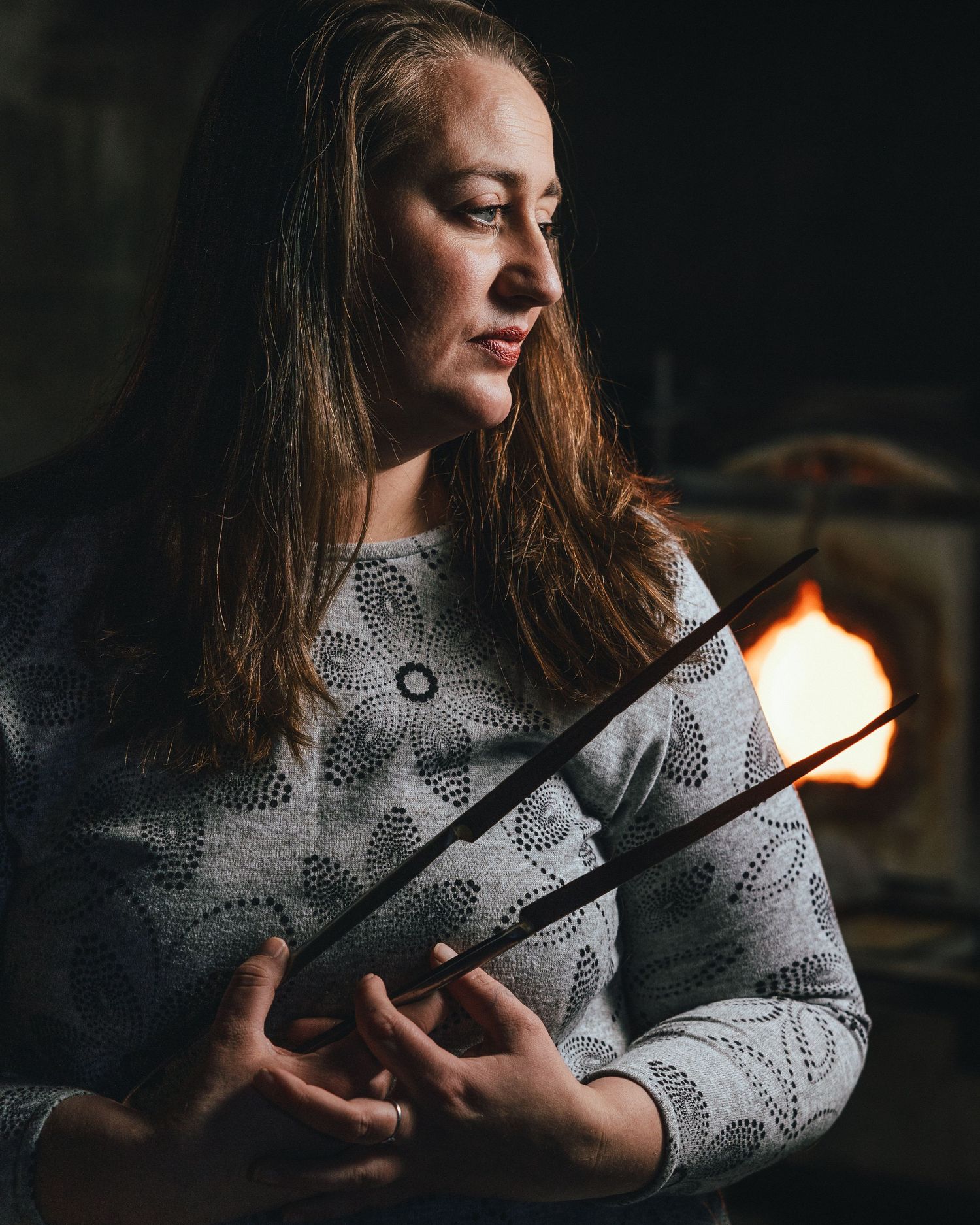 In moody lighting, someone in a patterned sweater holds chopsticks while gazing to the side in a contemplative pose.