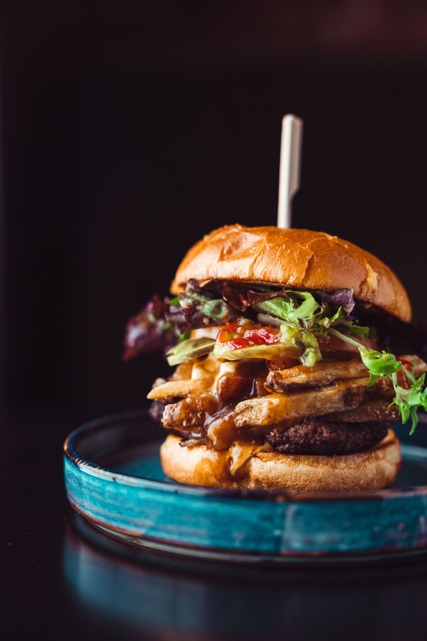 Juicy gourmet burger with sauteed mushrooms and lettuce served on a bright blue plate against a dark background.