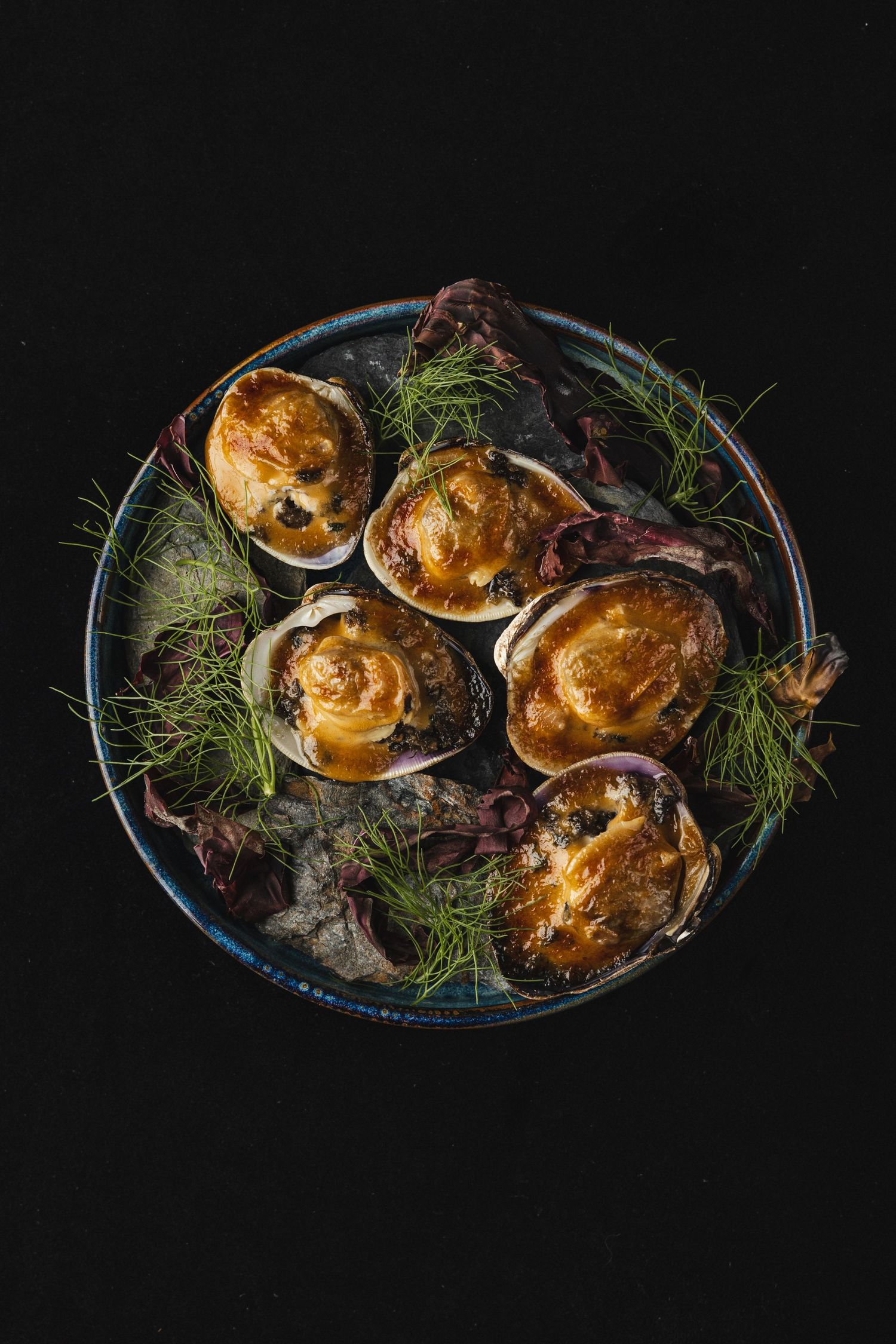Golden puff pastry appetizers garnished with fresh dill and purple microgreens on a dark ceramic plate.