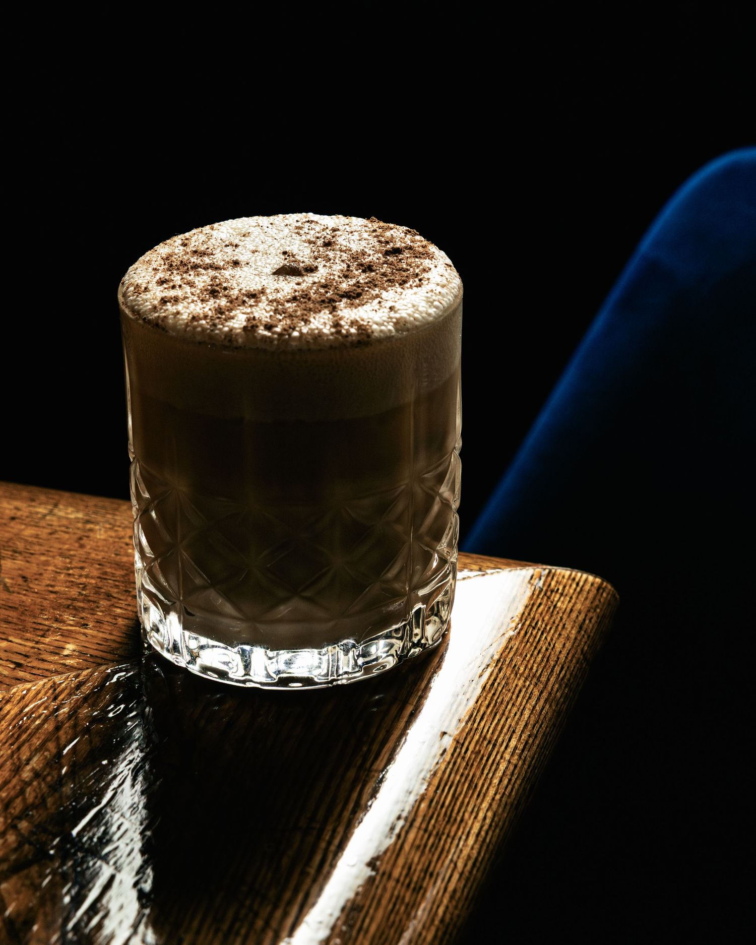 A rich coffee cocktail with frothy top and cocoa powder in a cut crystal glass.