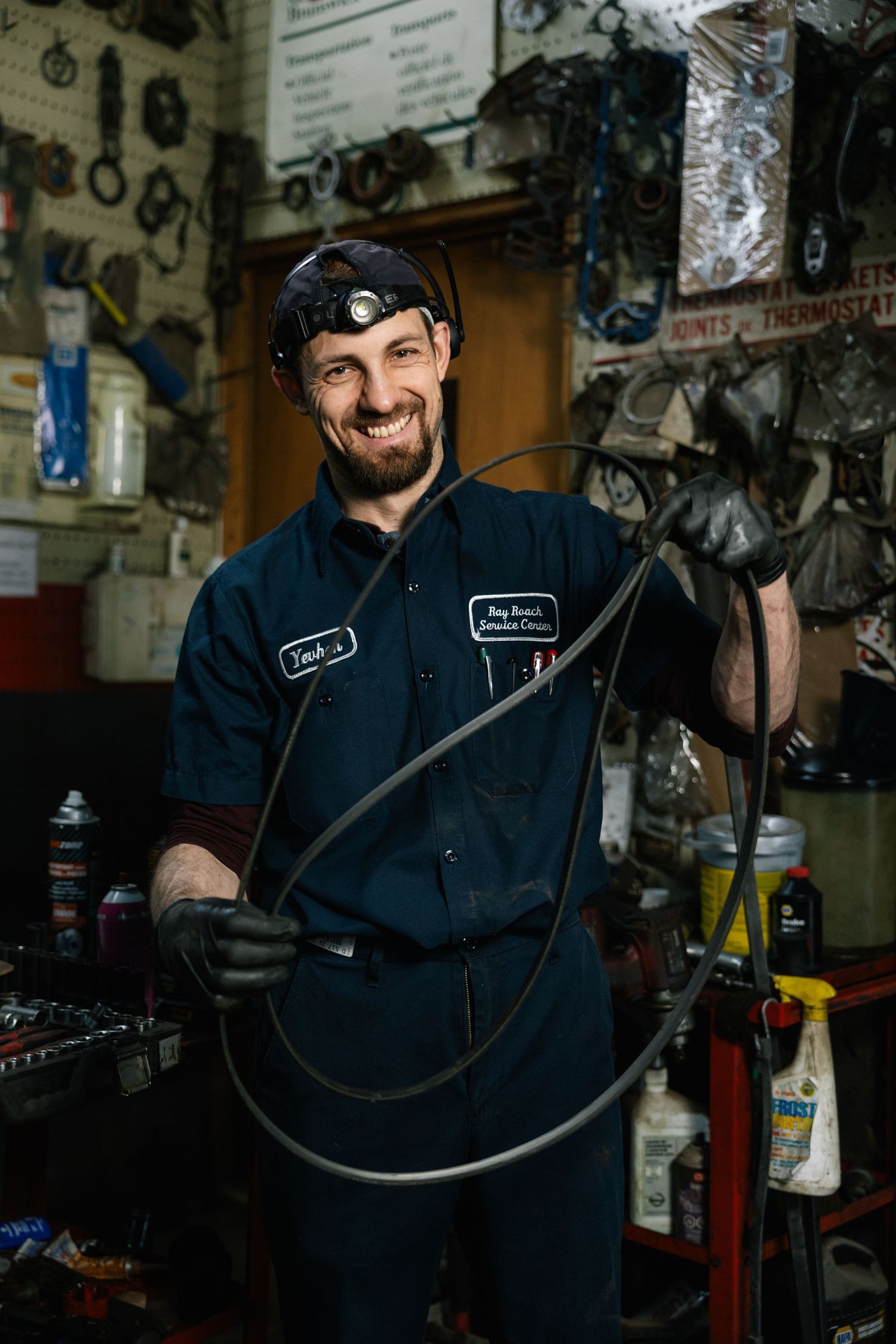 A mechanic in navy blue coveralls works in an auto repair shop surrounded by tools and equipment.